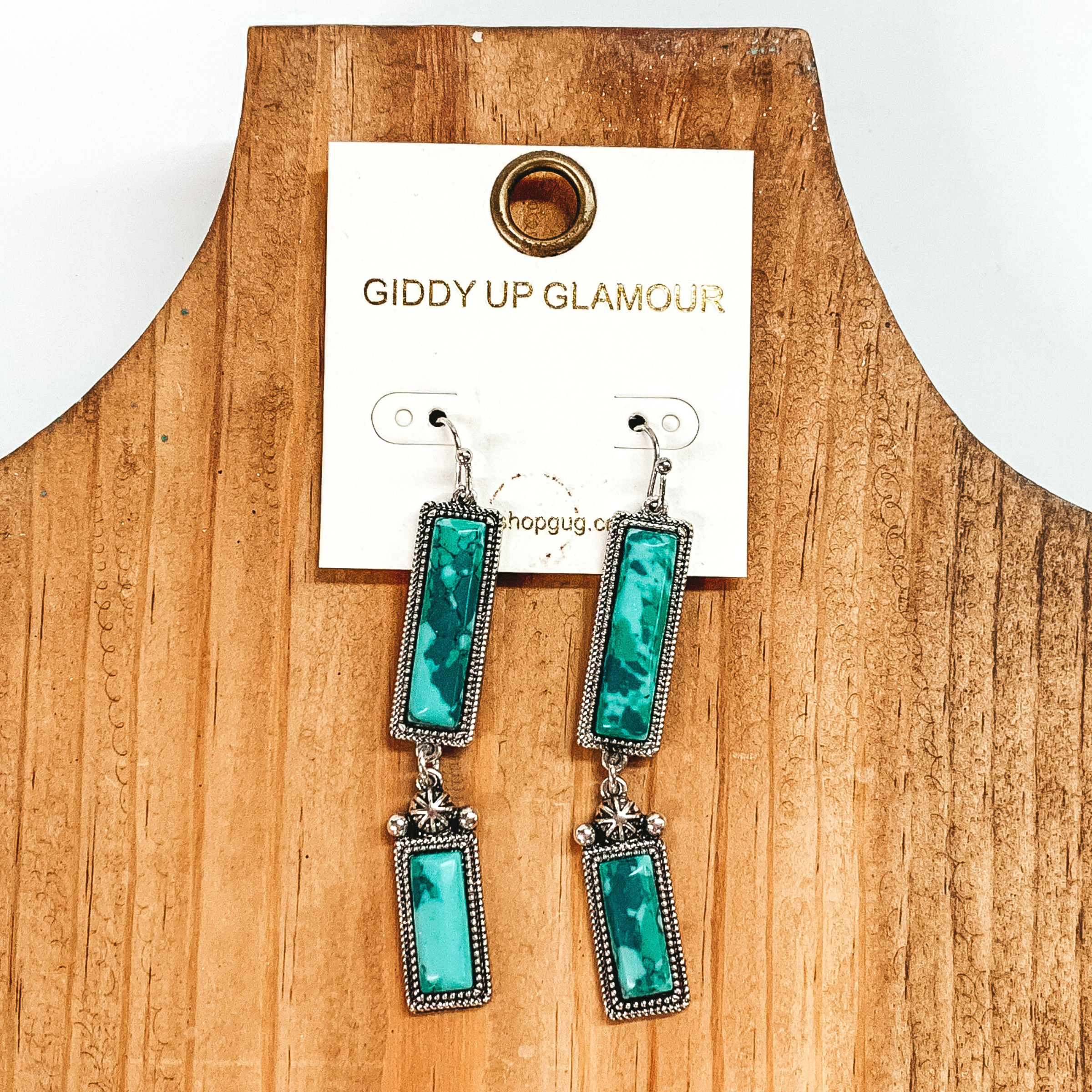 Silver drop earrings with two silver, rectangle drop. These earrings also include faux green stones. These earrings are pictured on a white and black picture. 