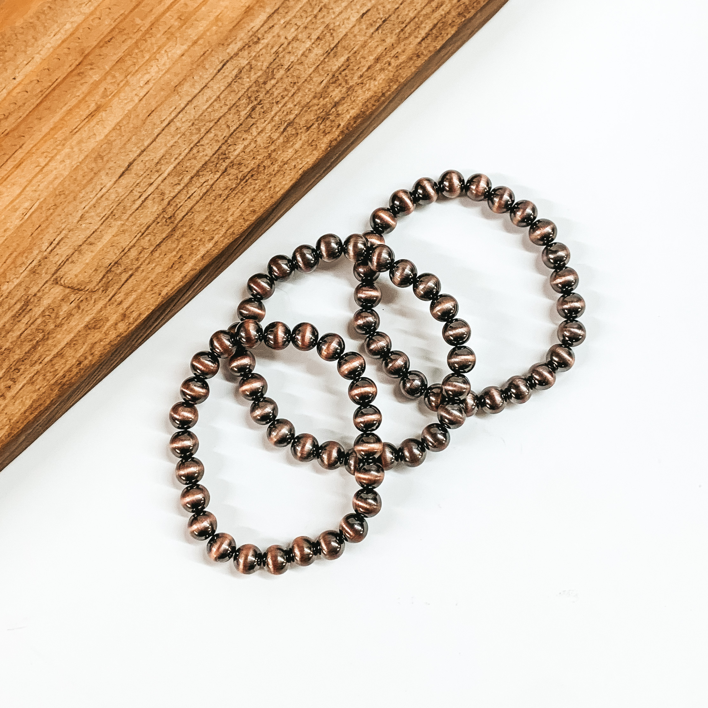Set of three copper beaded braceletes. These bracelets are pictured on a white background with a tan block of wood in the top left corner. 