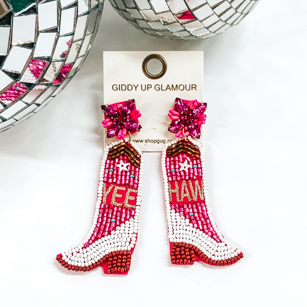 White and fuchsia beaded boot earrings. The word "YEE" and "HAW' are stitched one on each earring. These earrings are pictured on a white background with disco balls at the top.