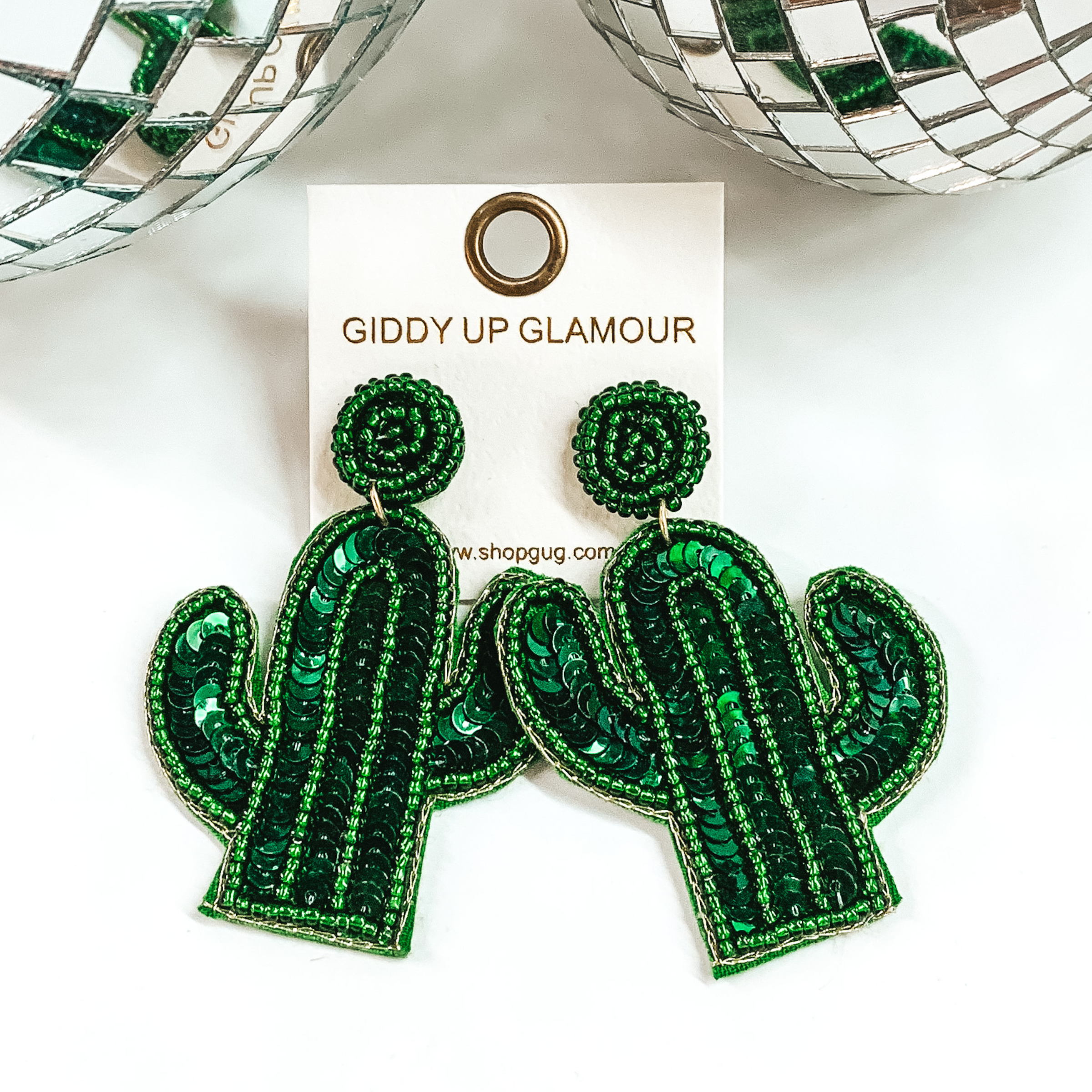 Green sequein cactus earrings with a green beaded outline. These earrings are pictured on a white background with disco balls at the top. 