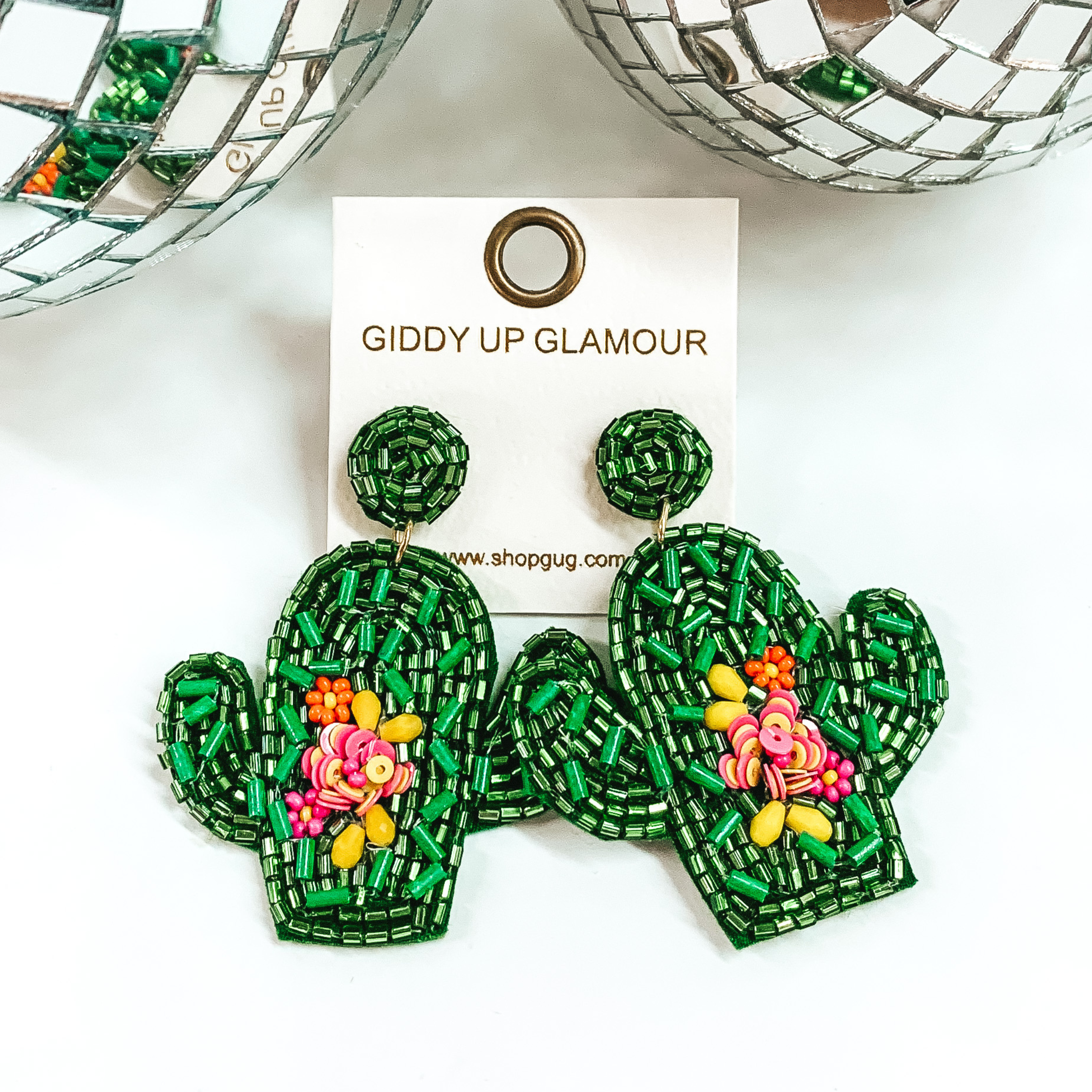 Green beaded cactus earrings with beaded, colorful flower design. These earrings are pictured on a white background with disco balls at the top. 