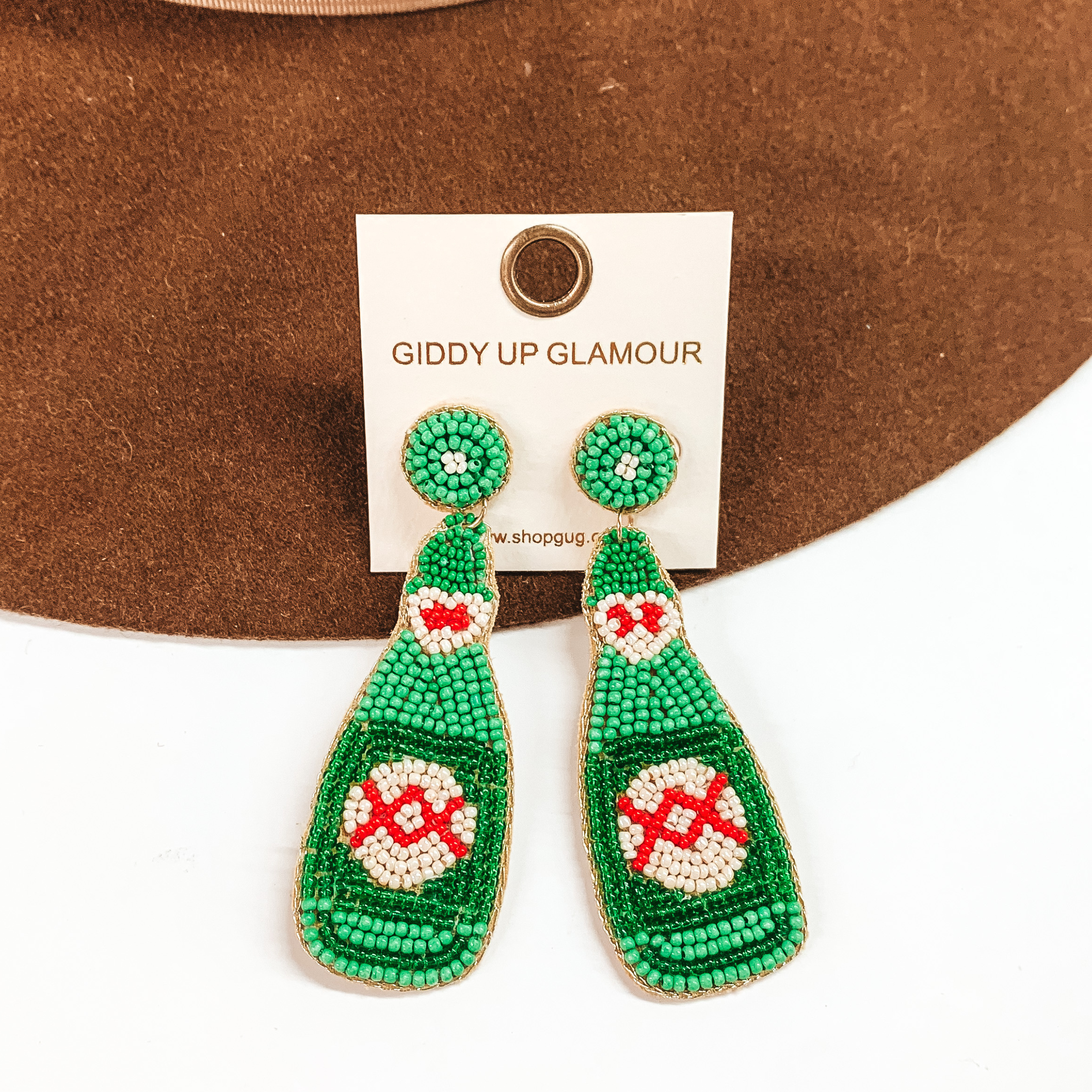 Green beaded bottle earrings with a white and red beaded design. These earrings are pictured on a white and brown background.