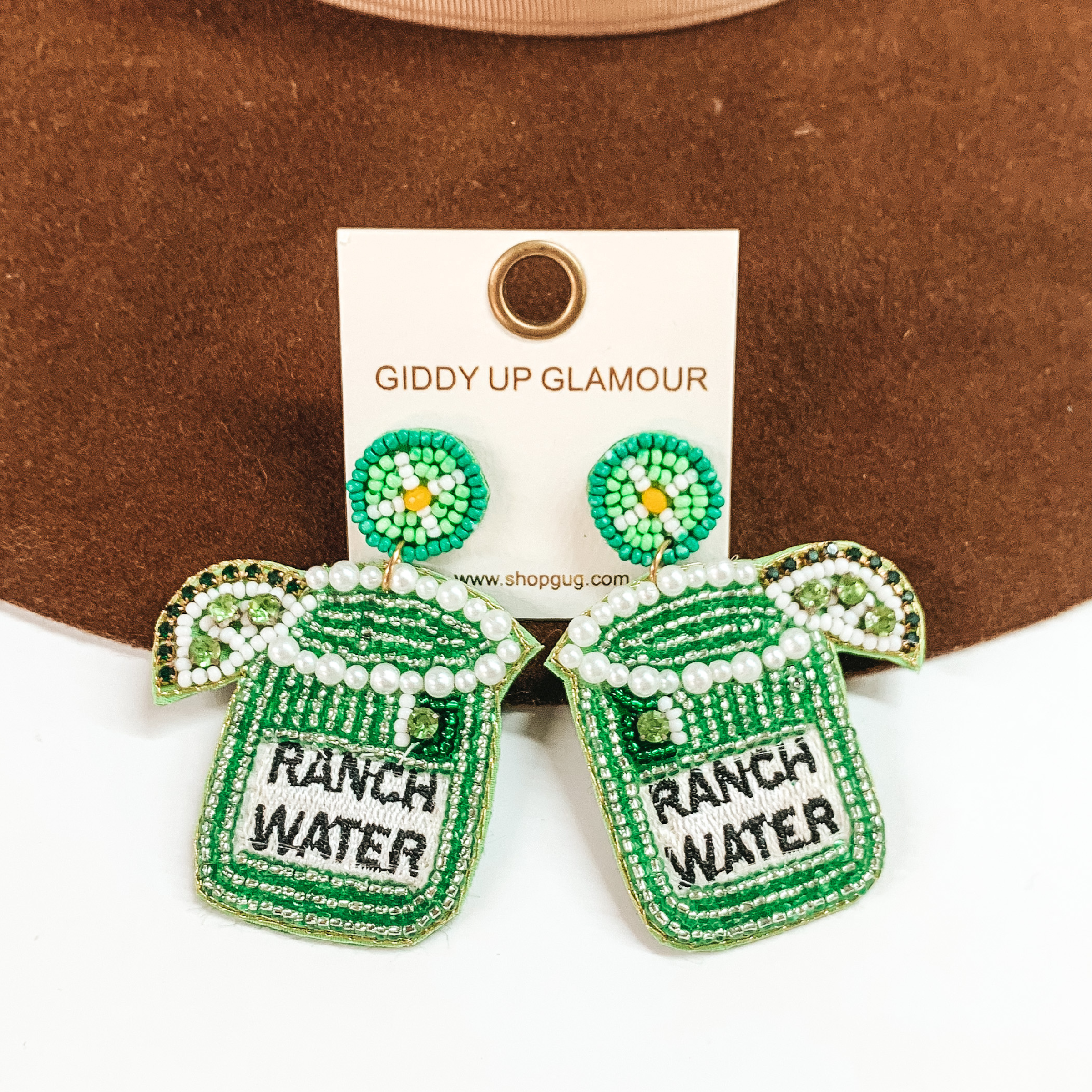 Green beaded coctail glass earrings. These earrings include a lime and the words"RANCH WATER" stitched in black. These earrings are pictured on a white and brown background.