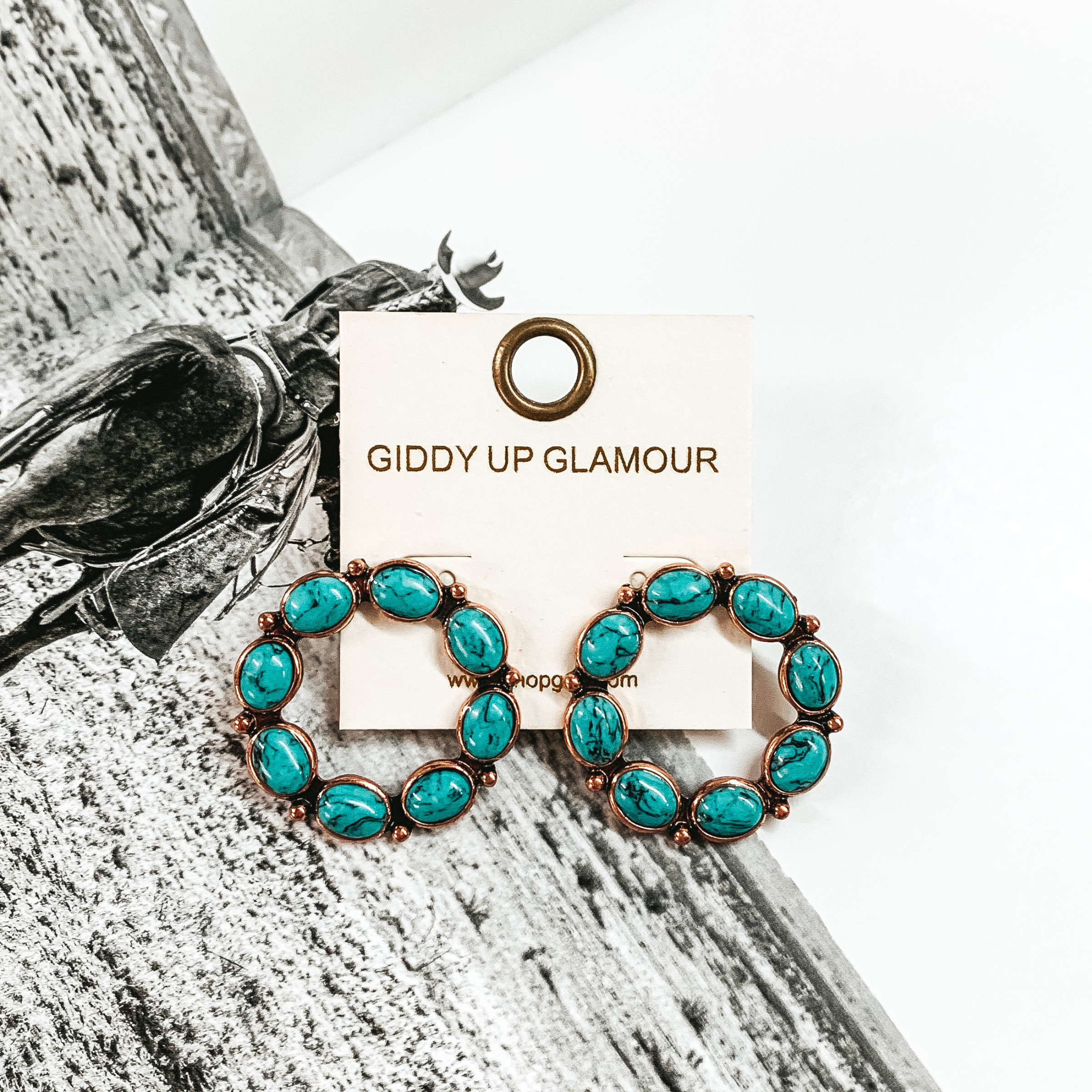 Open circle copper earrings that are outlined in turquoise stones. These earrings are pictured on a black and white picture. 