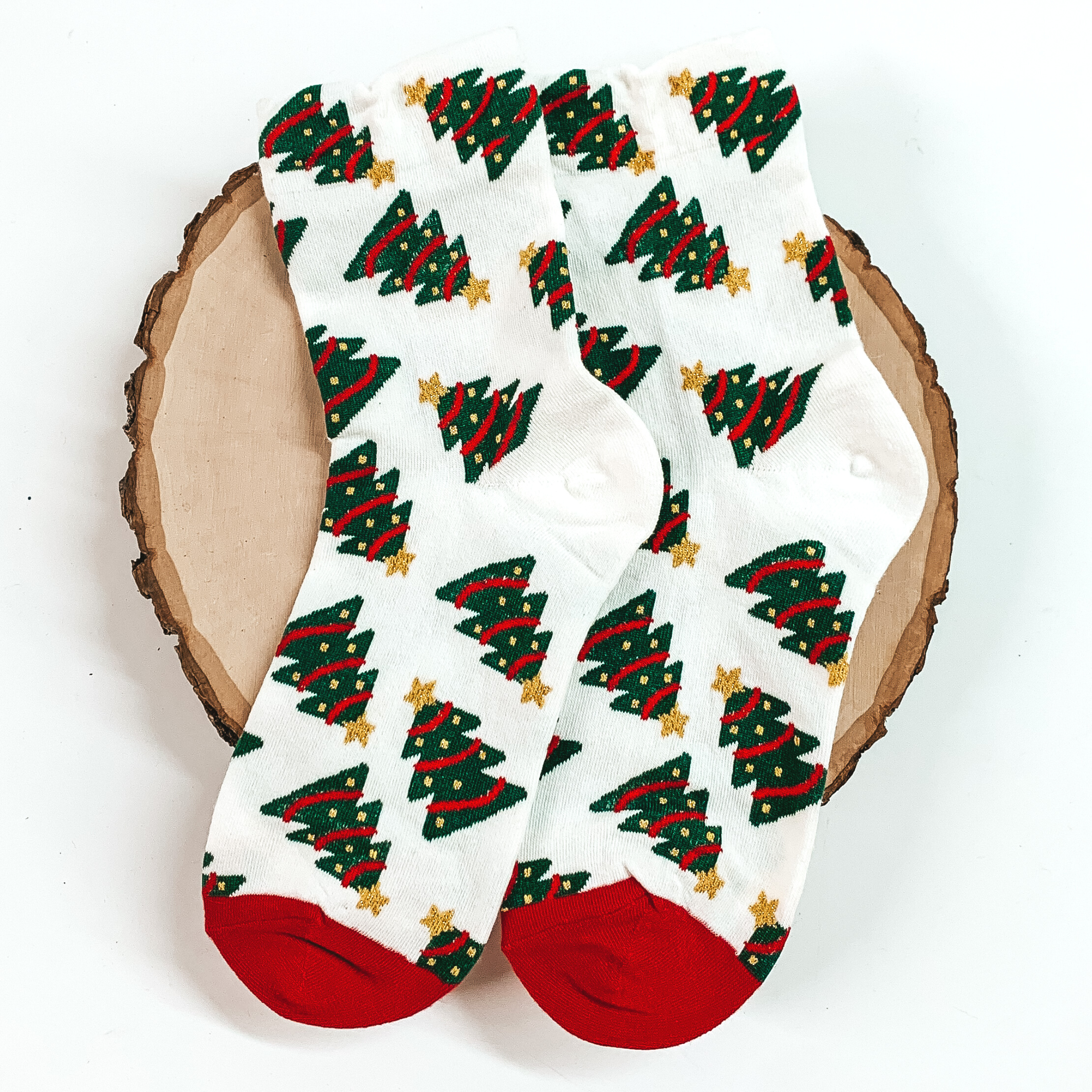 White ankle socks with red toes and a christmas tree design. These socks are pictured on a piece of wood on a white background. 