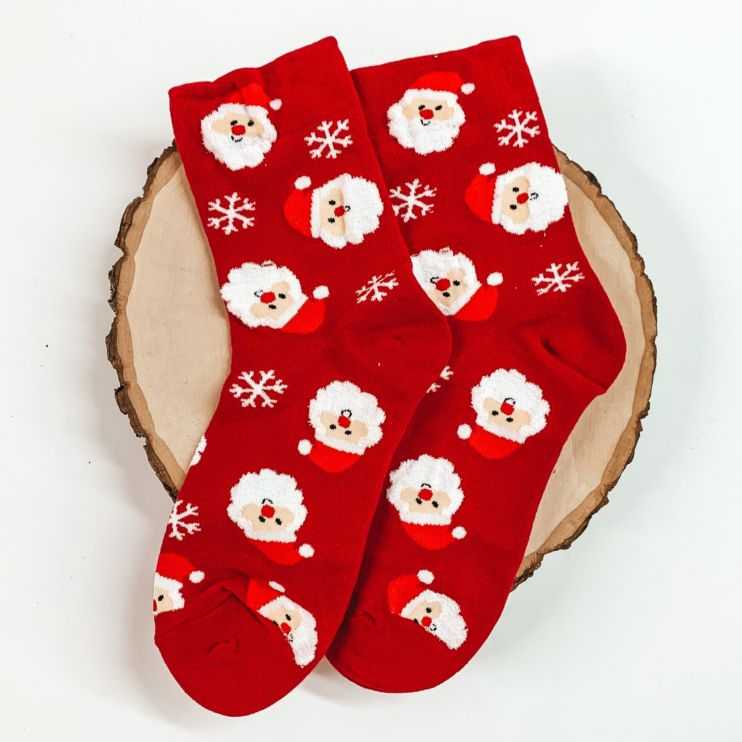 Red ankle socks with a santa claus head and snowflake design. These socks are pictured on a piece of wood on a white background. 