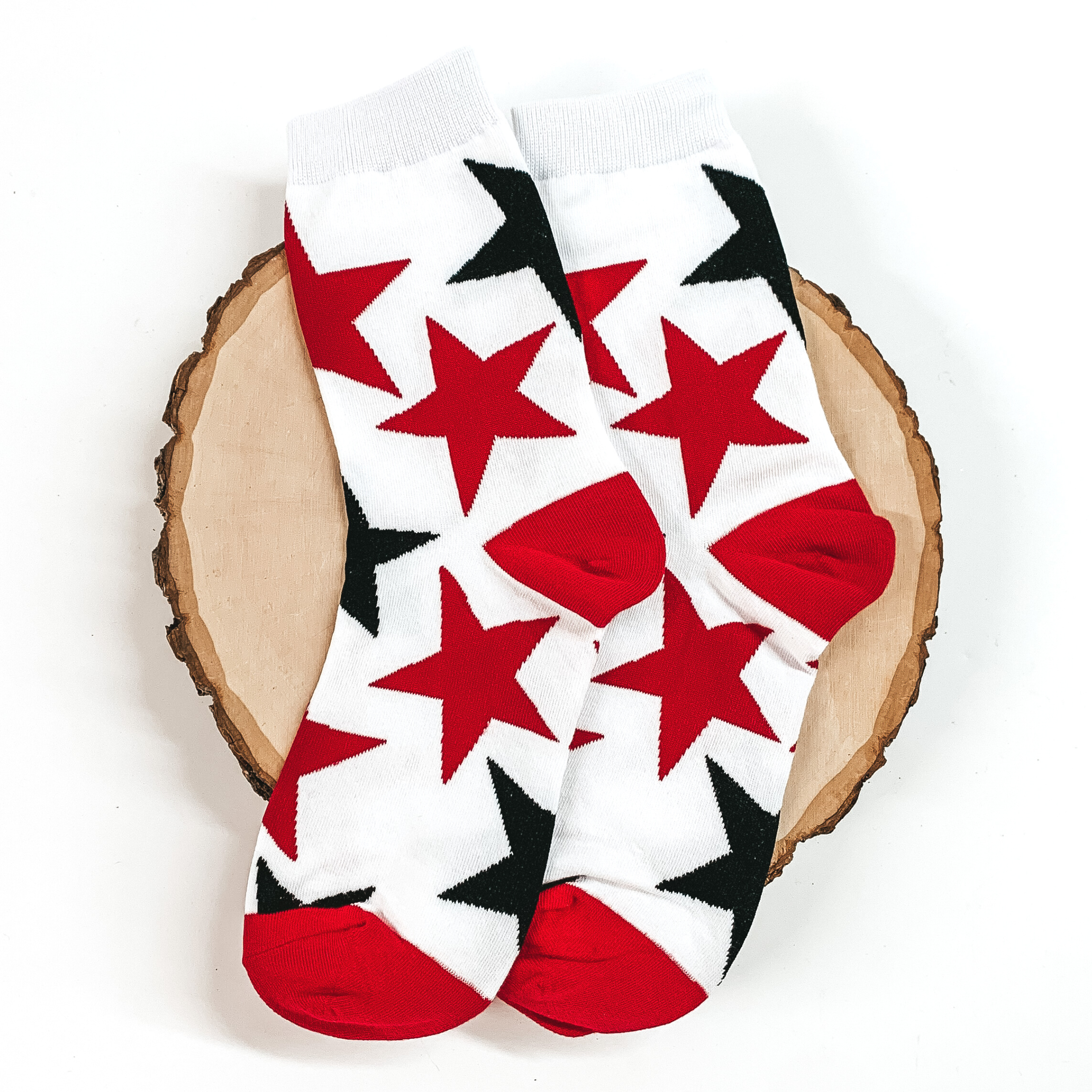 White ankle socks with a black and red star print. These socks are pictured on a piece of wood on a white background. 