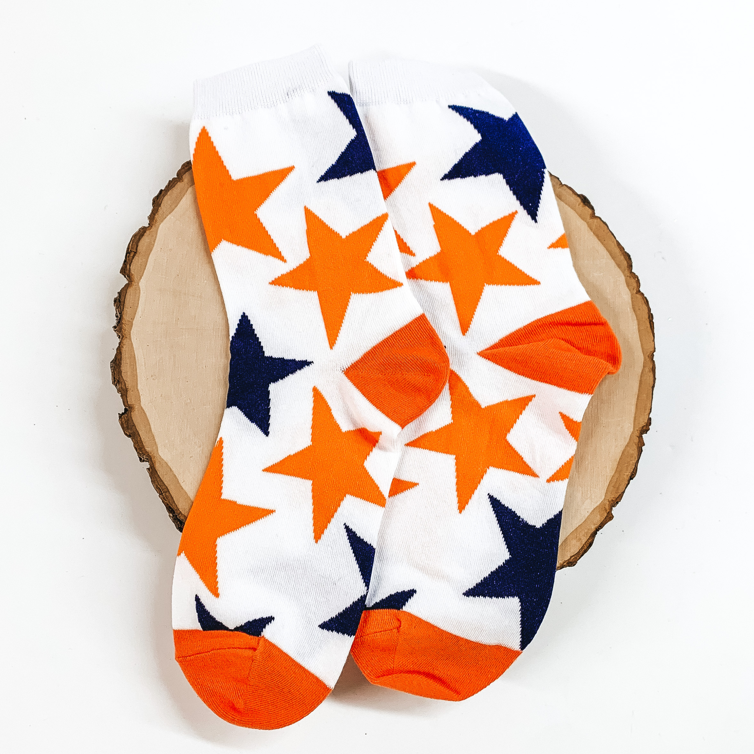 White ankle socks with a navy and orange star print design. These socks are pictured on a piece of wood on a white background. 