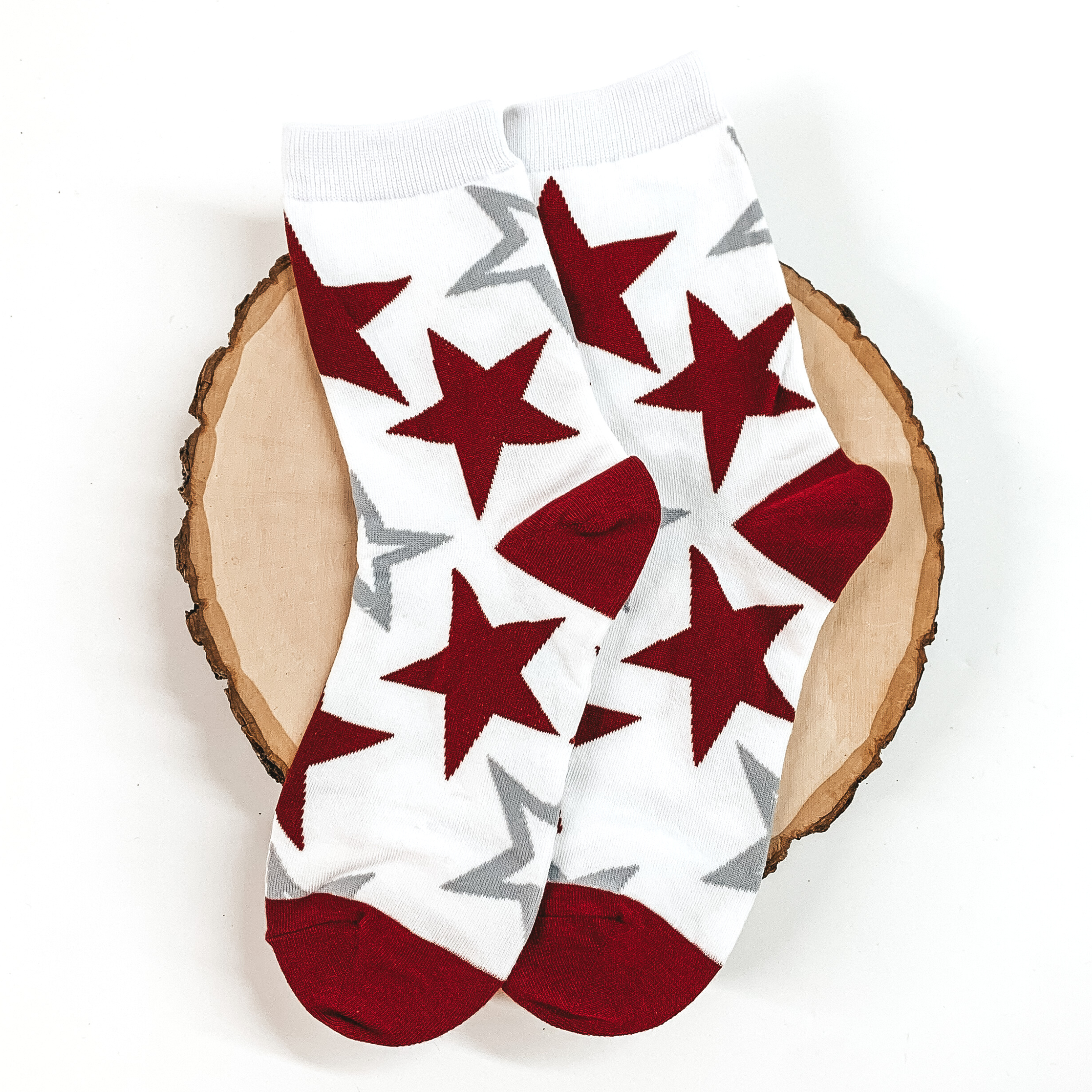White ankle socks with a maroon and grey star print. These socks are pictured on a piece of wood on a white background. 