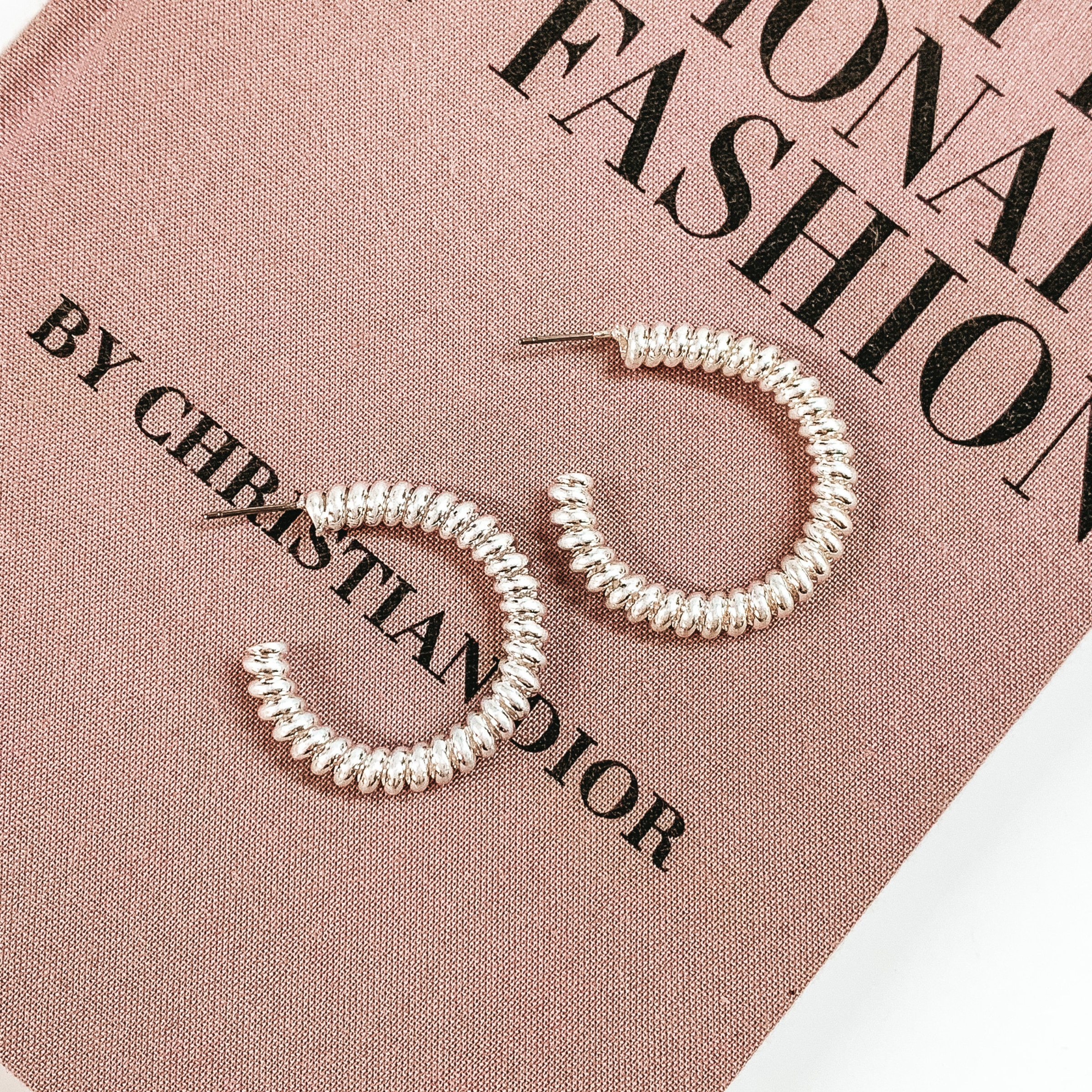 Silver, spiral hoop earrings pictured on a mauve colored book on a white background. 