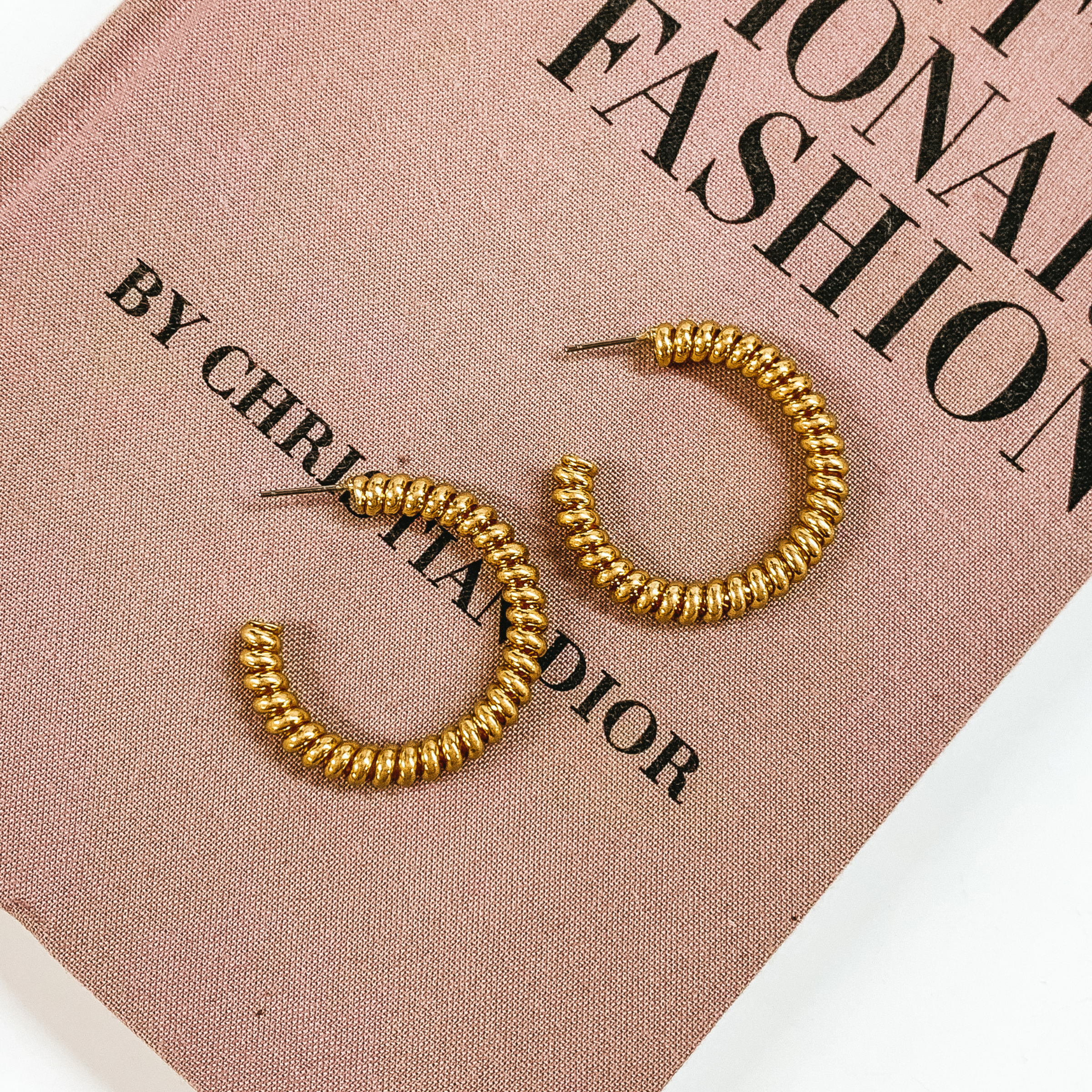 Gold, spiral hoop earrings pictured on a mauve colored book on a white background. 
