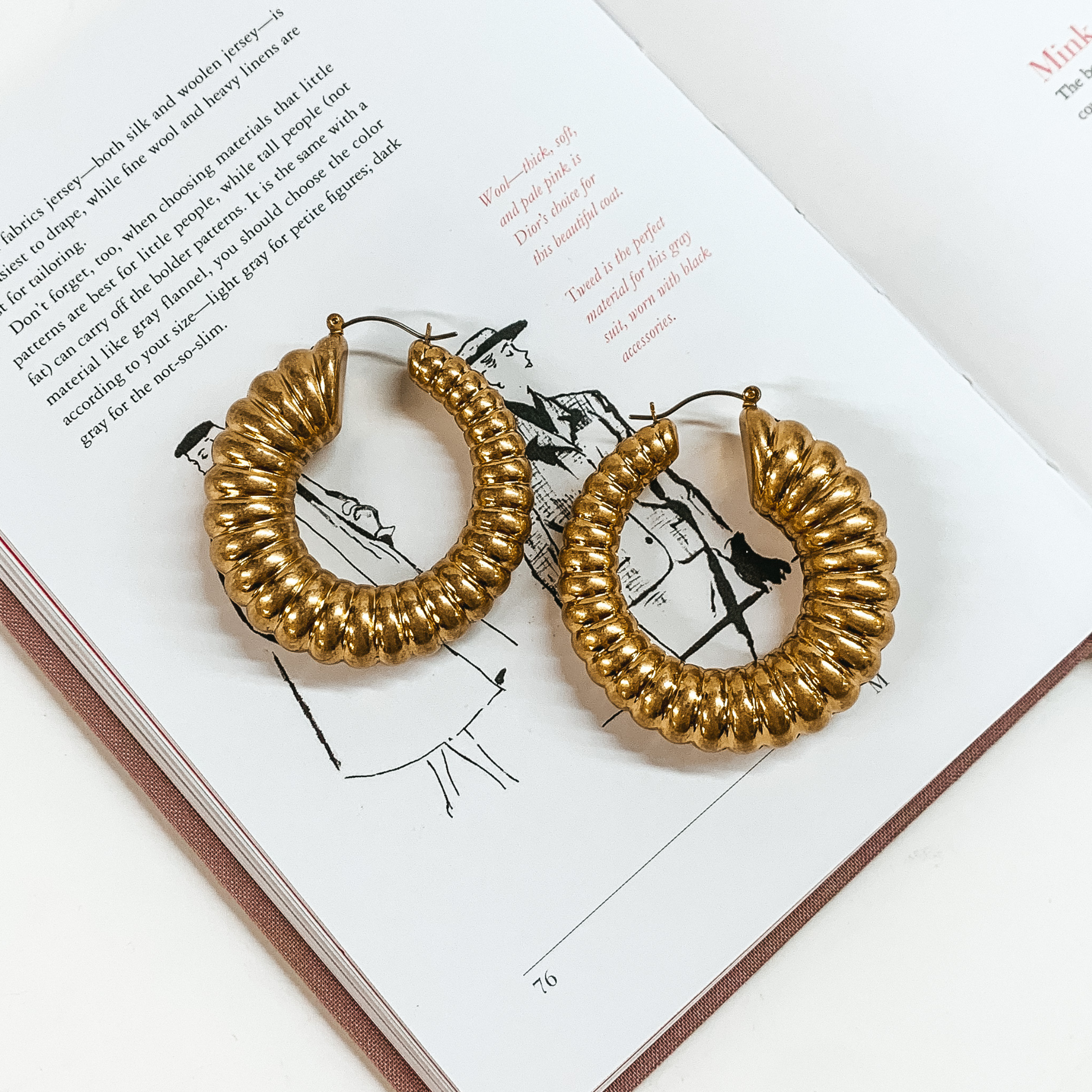 Gold hoop earrings pictured on top of an open book on a white background. 
