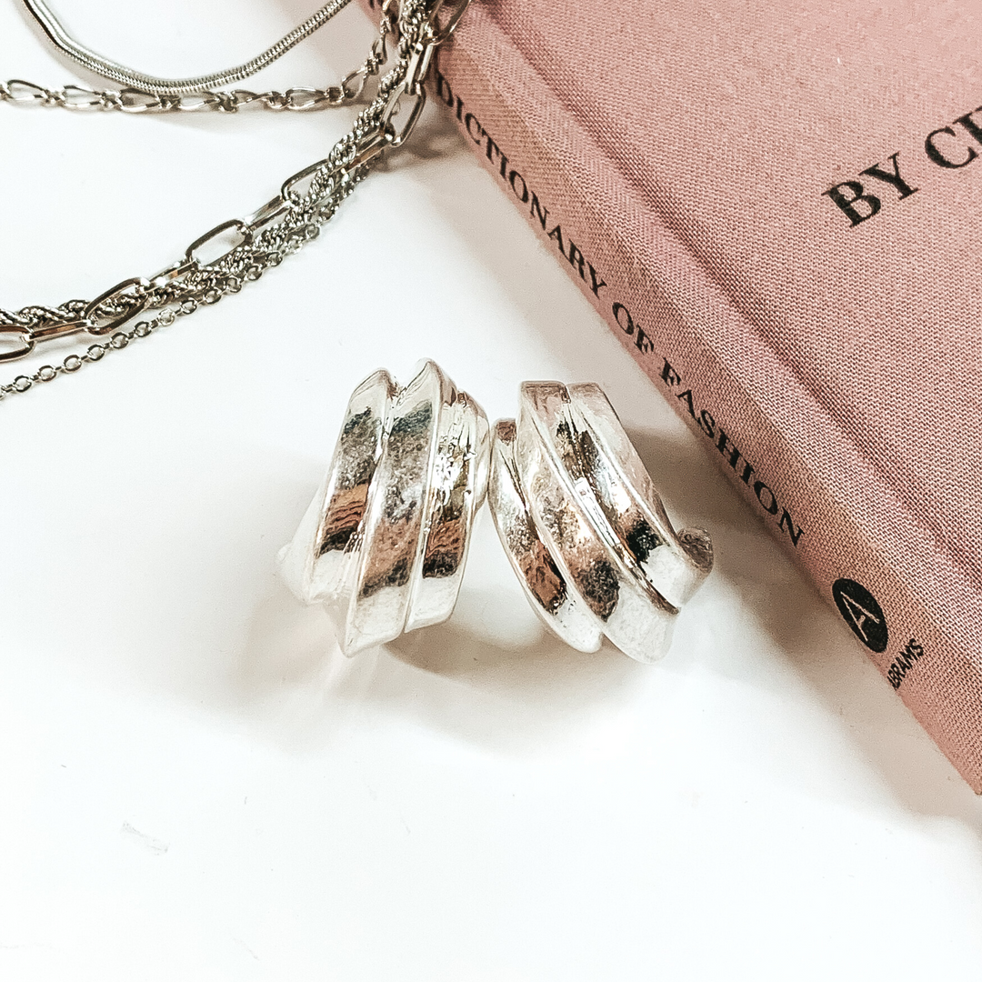 Silver, layered hoop earrings pictured on a white background with a mauve book and silver chains in the back of the picture. 
