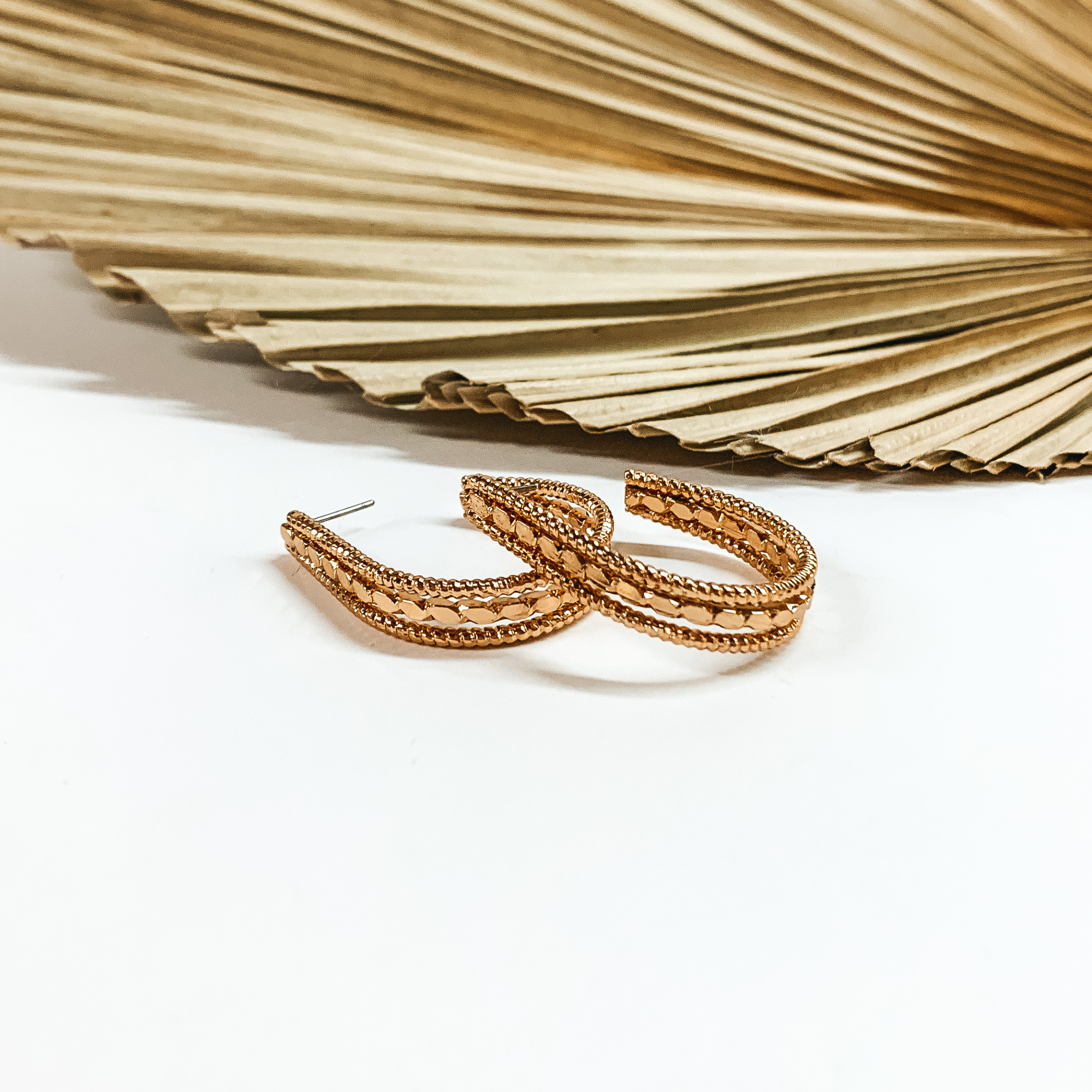 Teardrop, gold hoop earrings with different textures. These earrings are pictured in front a sage green leaf on a white background. 