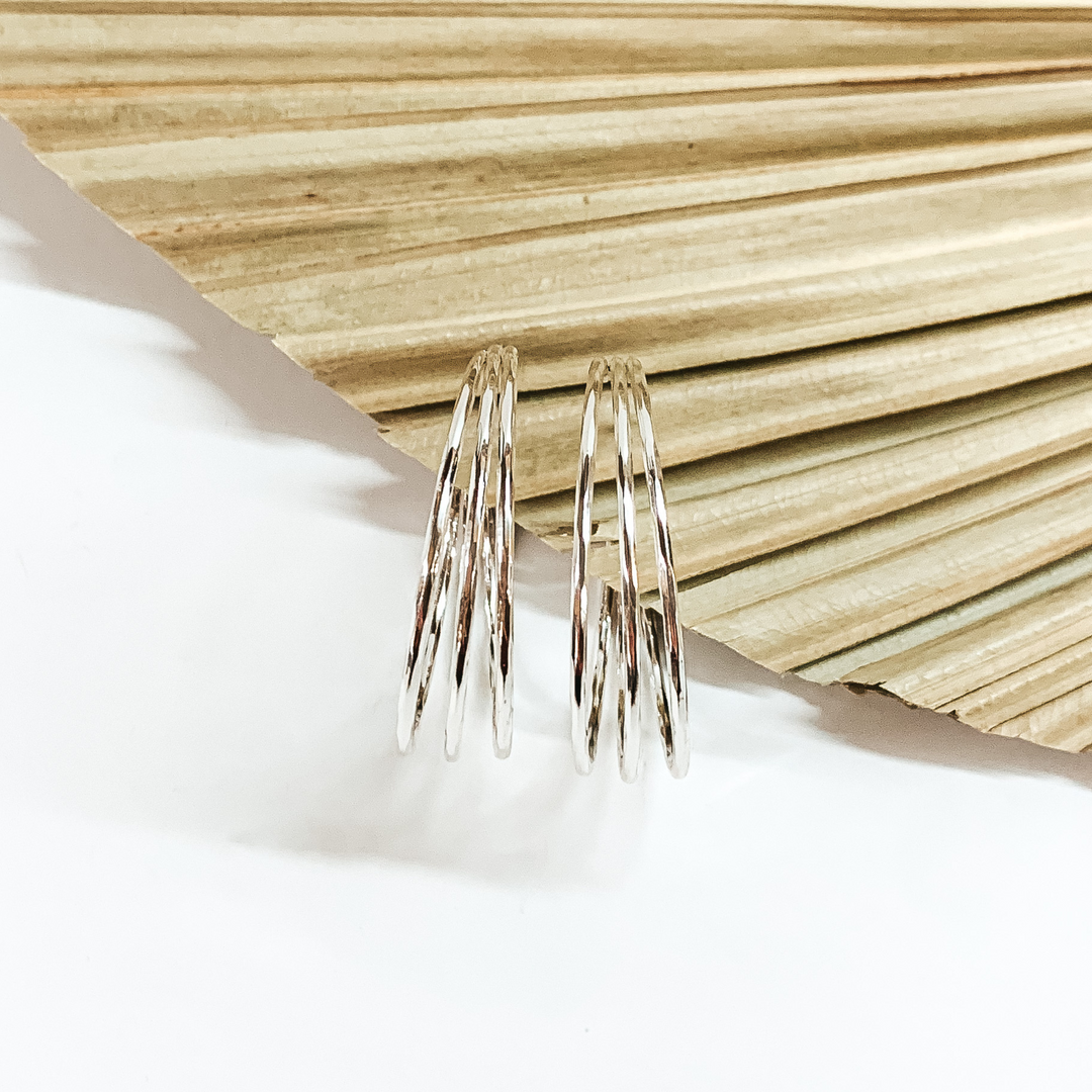 Triple, silver hoop earrings pictured in front a sage green leaf on a white background. 