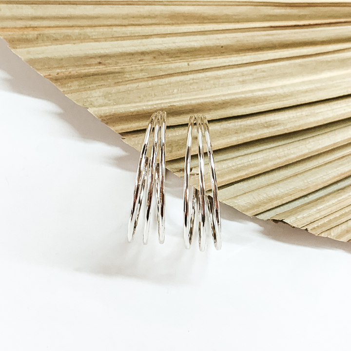 Triple, silver hoop earrings pictured in front a sage green leaf on a white background. 