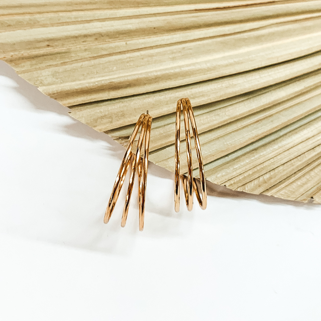 Triple, gold hoop earrings pictured in front a sage green leaf on a white background. 