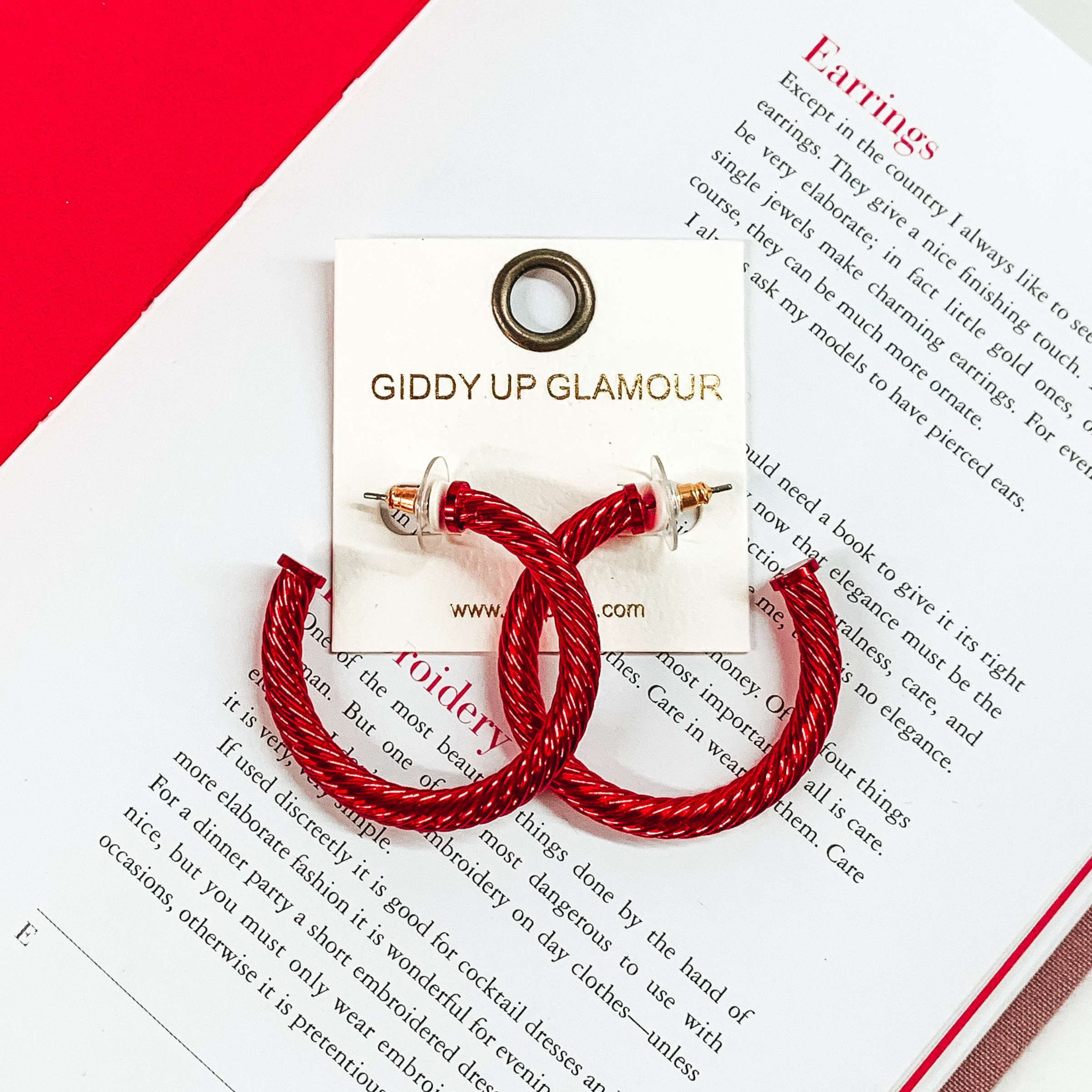Mettalic red cable hoop earrings pictured on an open book on a white background. 