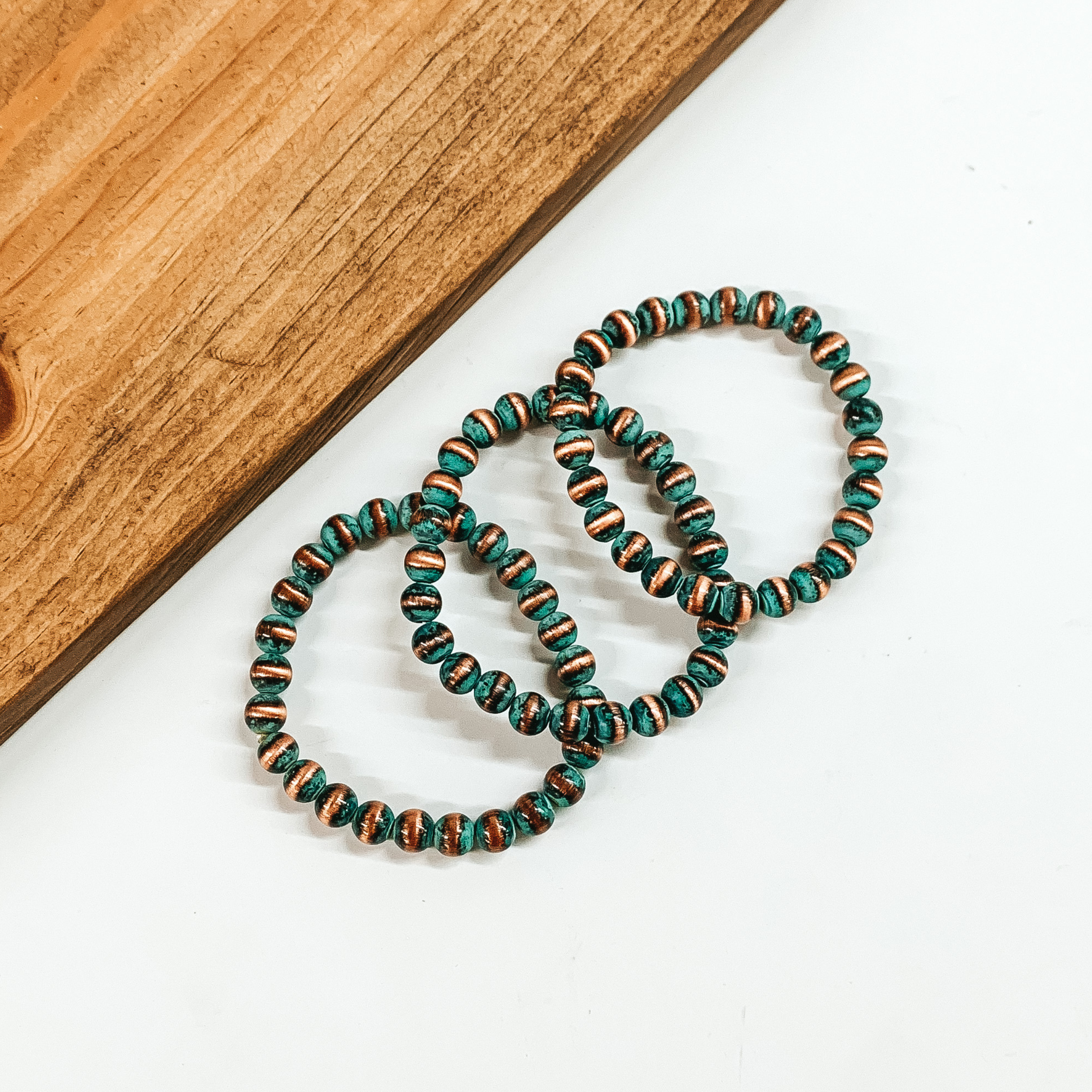 Set of three patina beaded braceletes. These bracelets are pictured on a white background with a tan block of wood in the top left corner. 