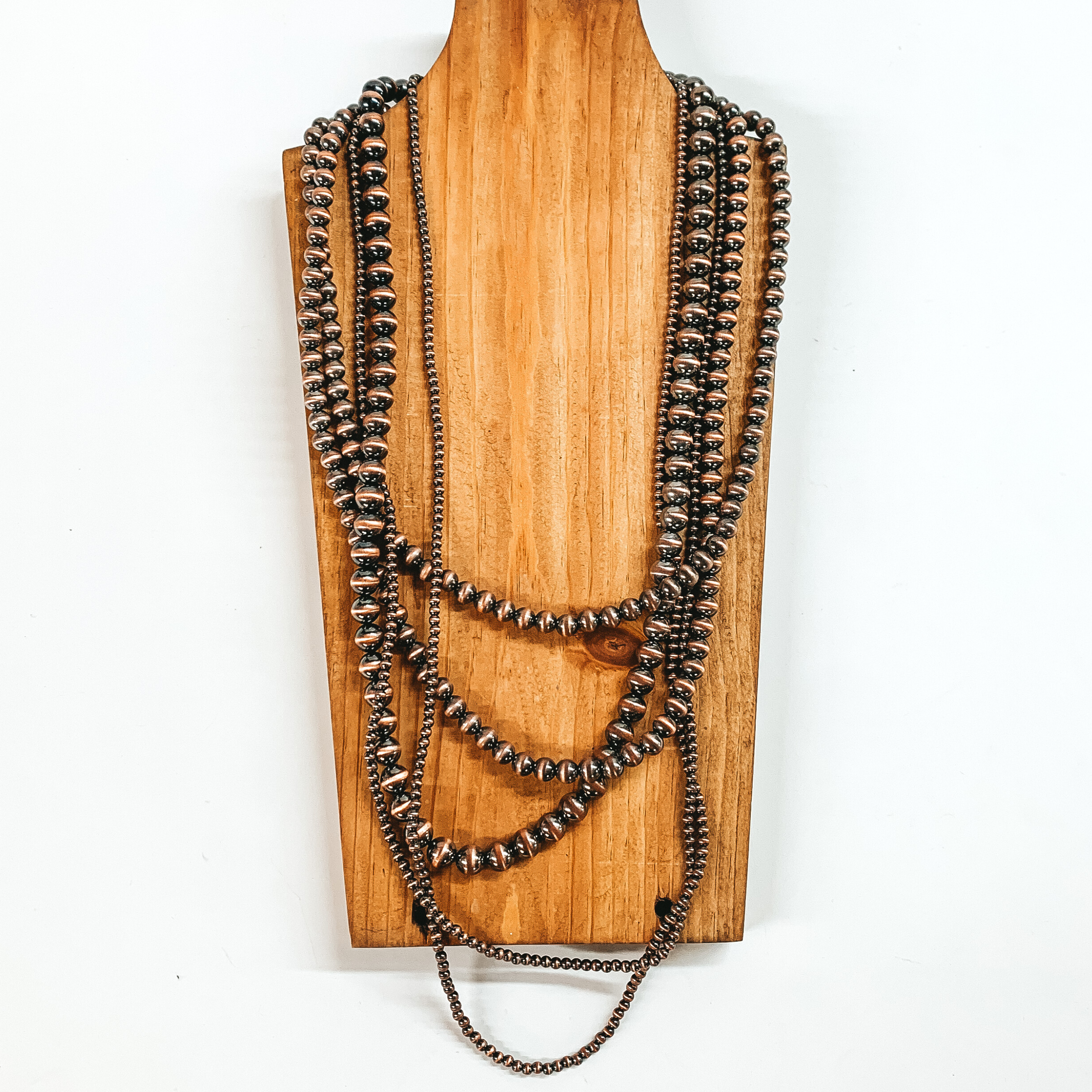 Five strand neckace with different sized copper beaded strands of different lengths. This necklace is pictured on a wooden necklace holder on a white background. 
