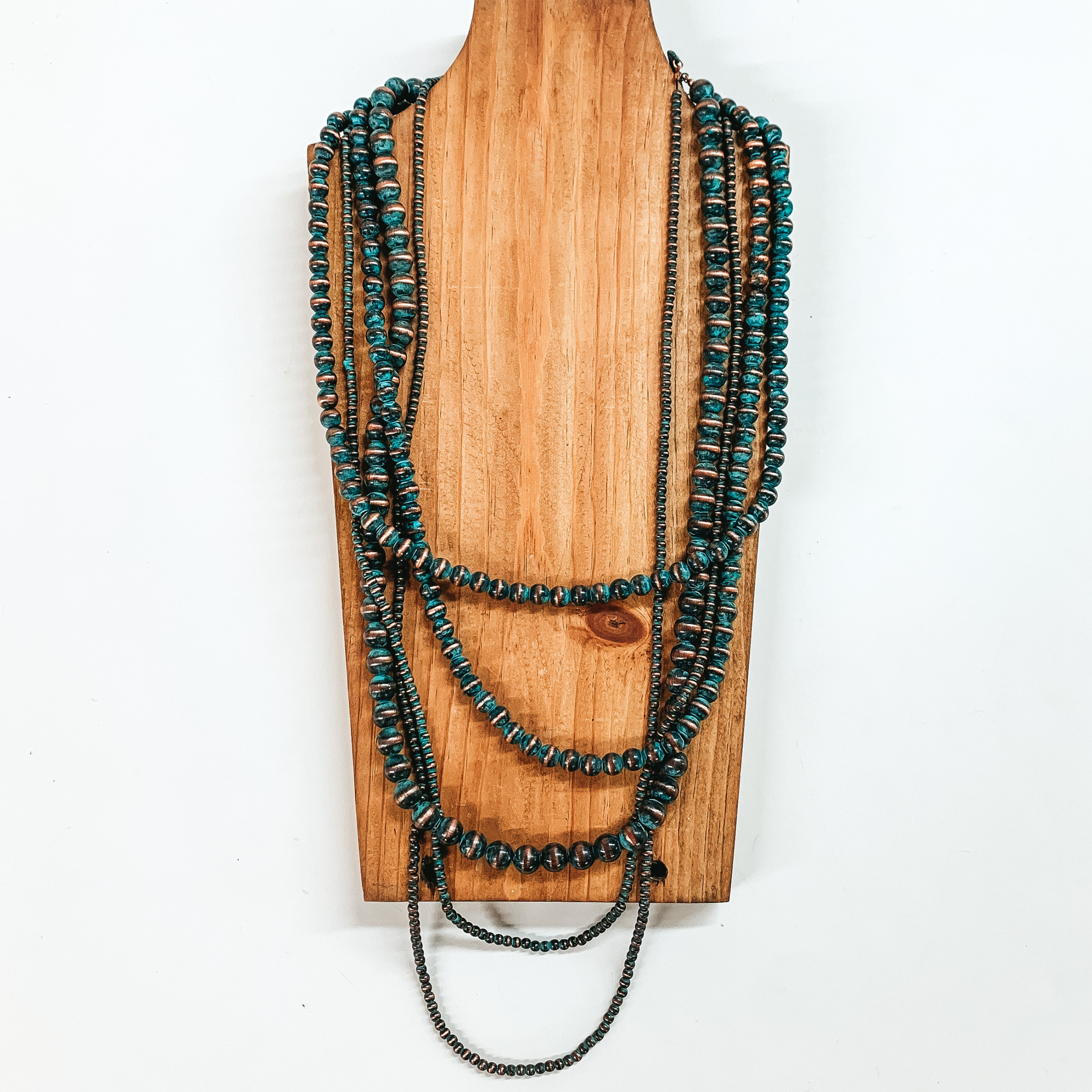 Five strand neckace with different sized patina beaded strands of different lengths. This necklace is pictured on a wooden necklace holder on a white background. 