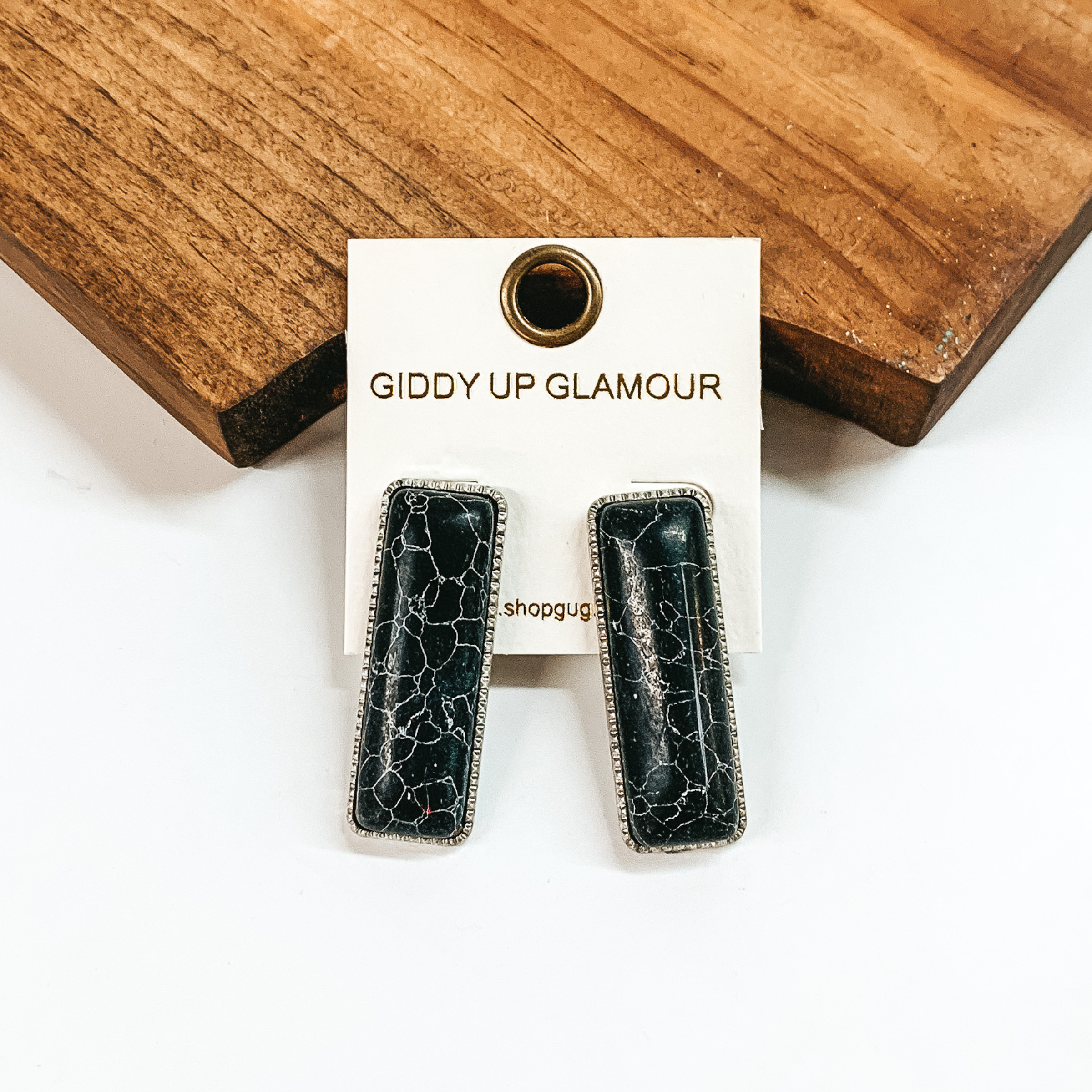 Rectangle, black stone earrings with a thin, silver outline. These earrings are pictured in front of a brown block on a white background. 