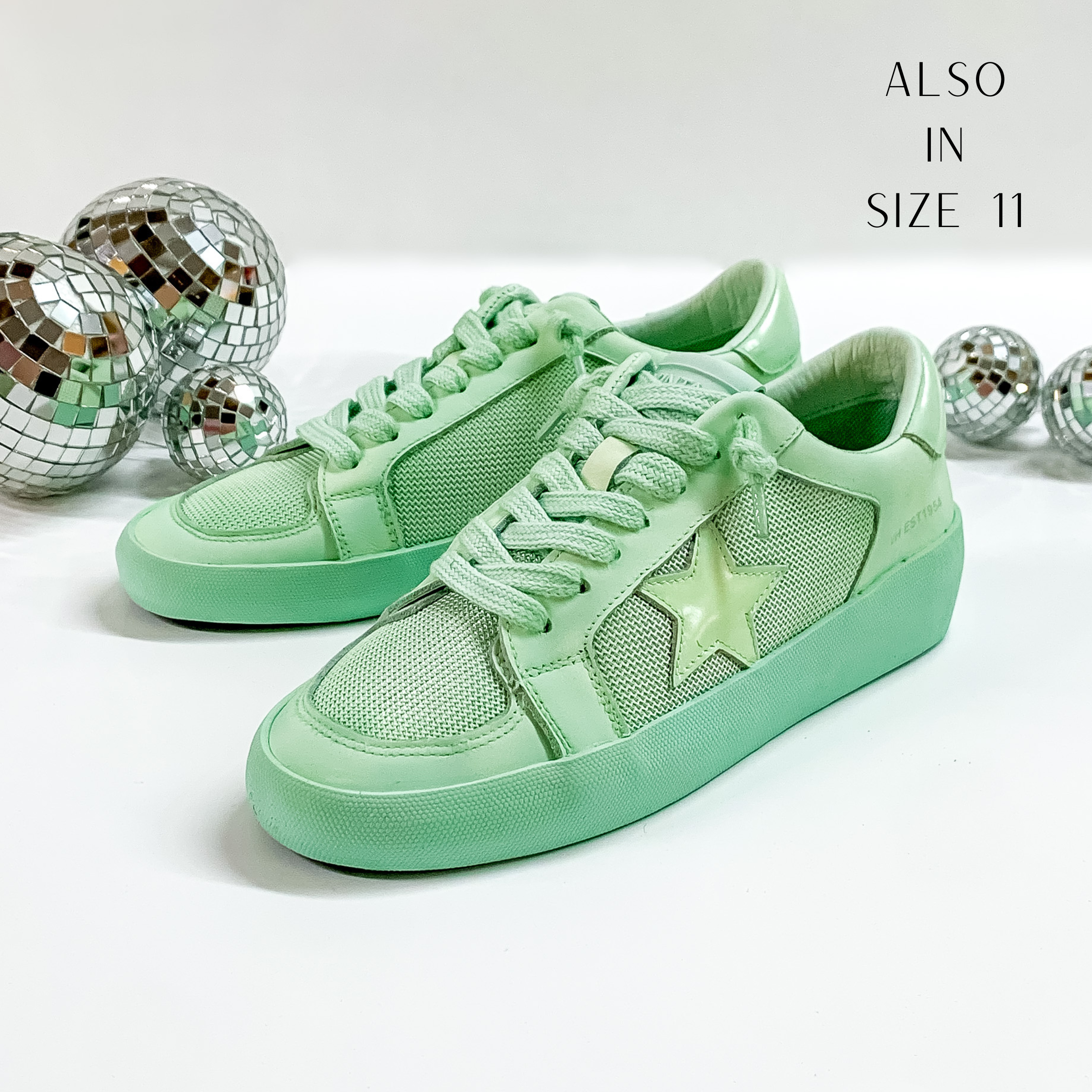 Mint green colored tennis shoes and shoelaces. The tennis shoes also have a mint green star patch on the side of the shoe. These shoes are pictured on a white background with disco balls behind them. 