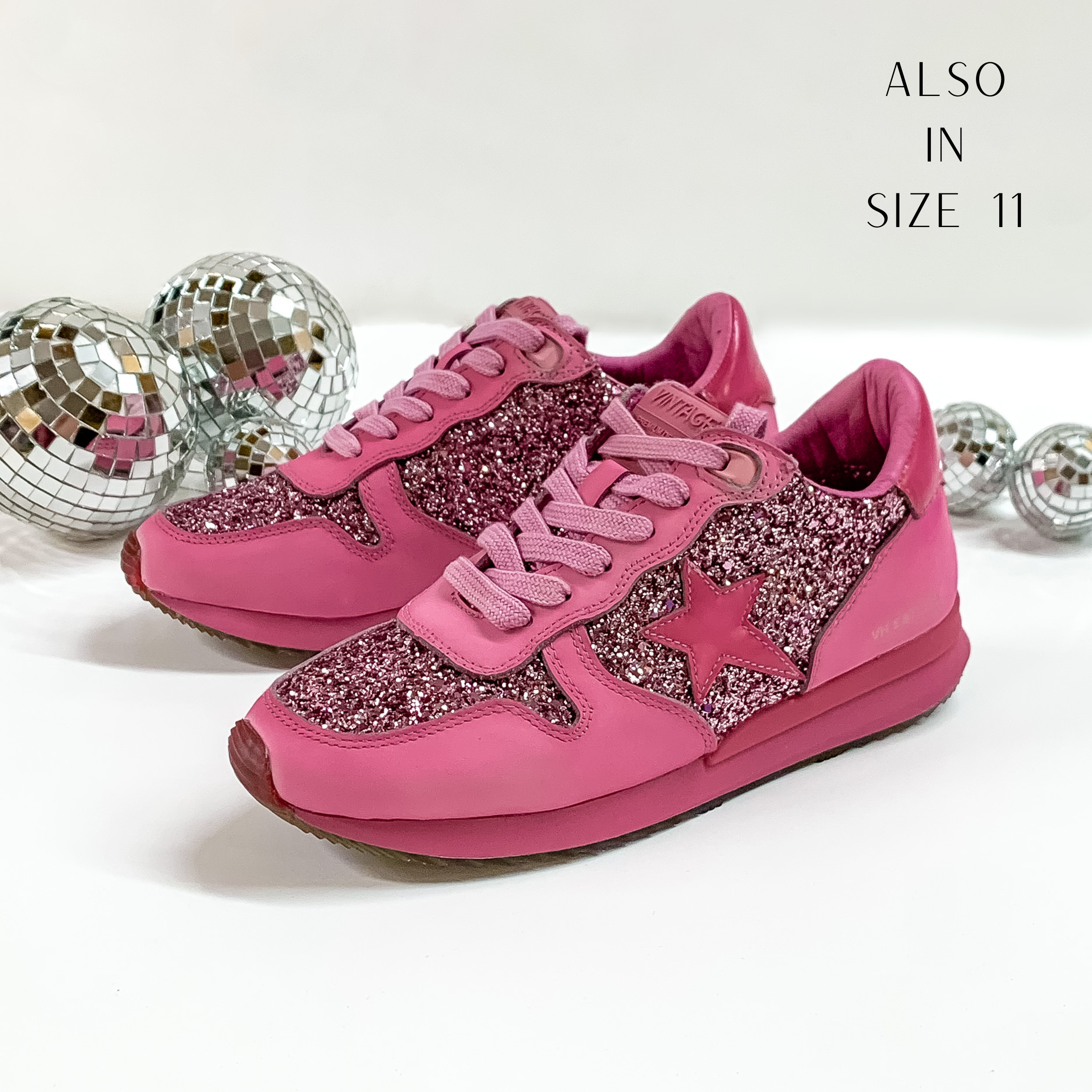 Dark pink colored tennis shoes and shoelaces. The tennis shoes also have a dark pink star patch on the side of the shoe and dark pink glitter throughout. These shoes are pictured on a white background with disco balls behind them. 