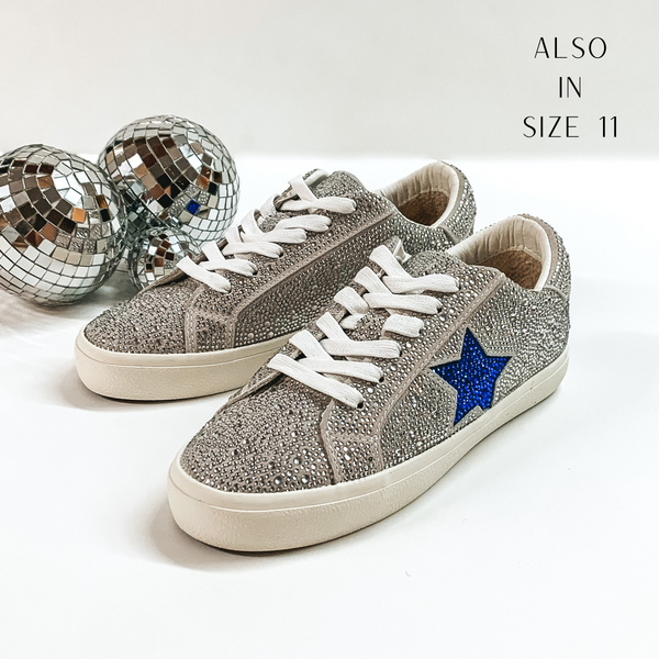 Silver crystal encrusted colored tennis shoes and white shoelaces. The tennis shoes also have a blue crystal star patch on the side. These shoes are pictured on a white background with disco balls behind them. 
