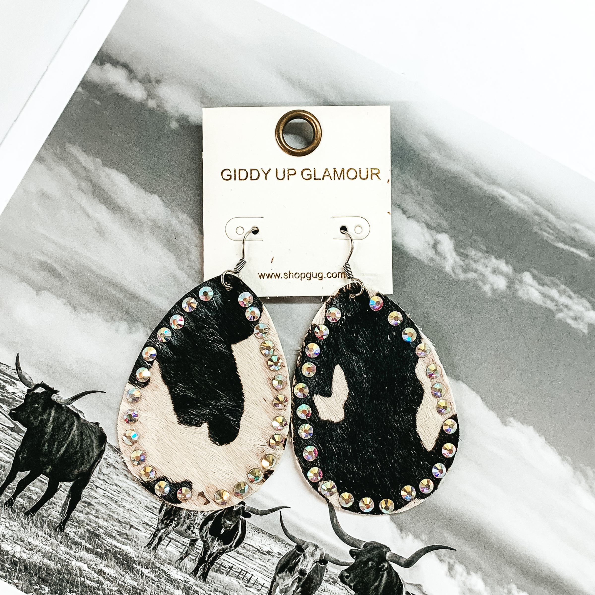Teardrop dangle earrings that look like a white and black cow print. These earrings also have an AB crystal outline. These earrings are pictured on a black and white picture of cows.