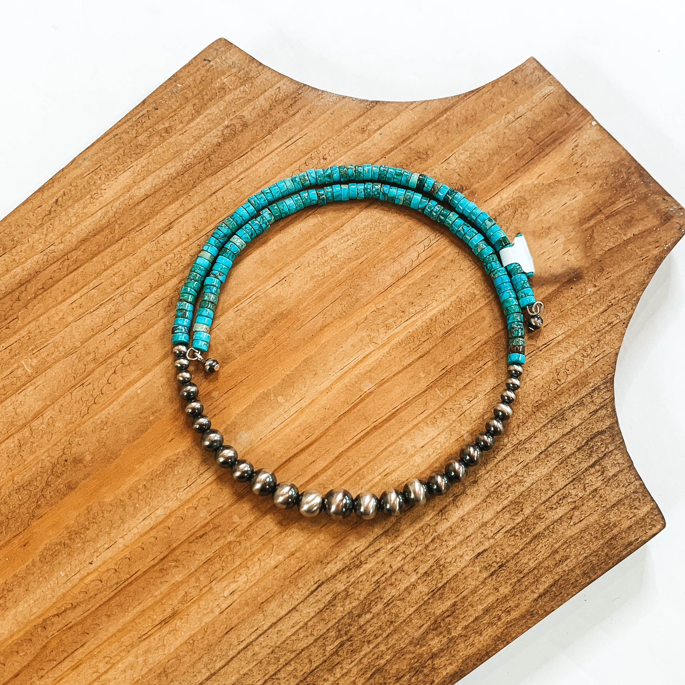 Half silver beaded and half turquoise beaded wrap necklace. This necklace is pictured on a wood necklace holder on a white background. 