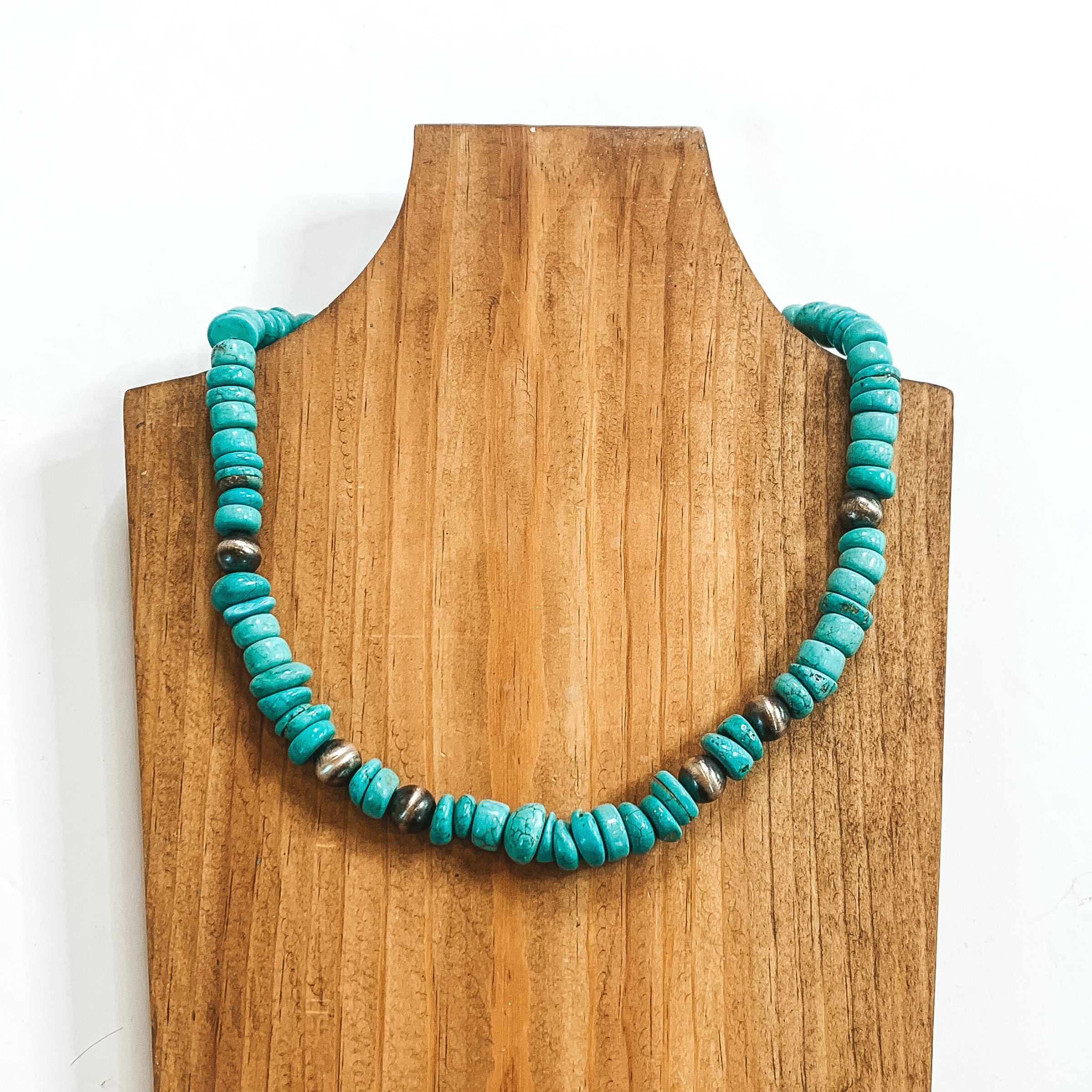 Turquoise chip beaded necklace with silver bead spacers. This necklace is pictured on a wood necklace holder on a white background. 