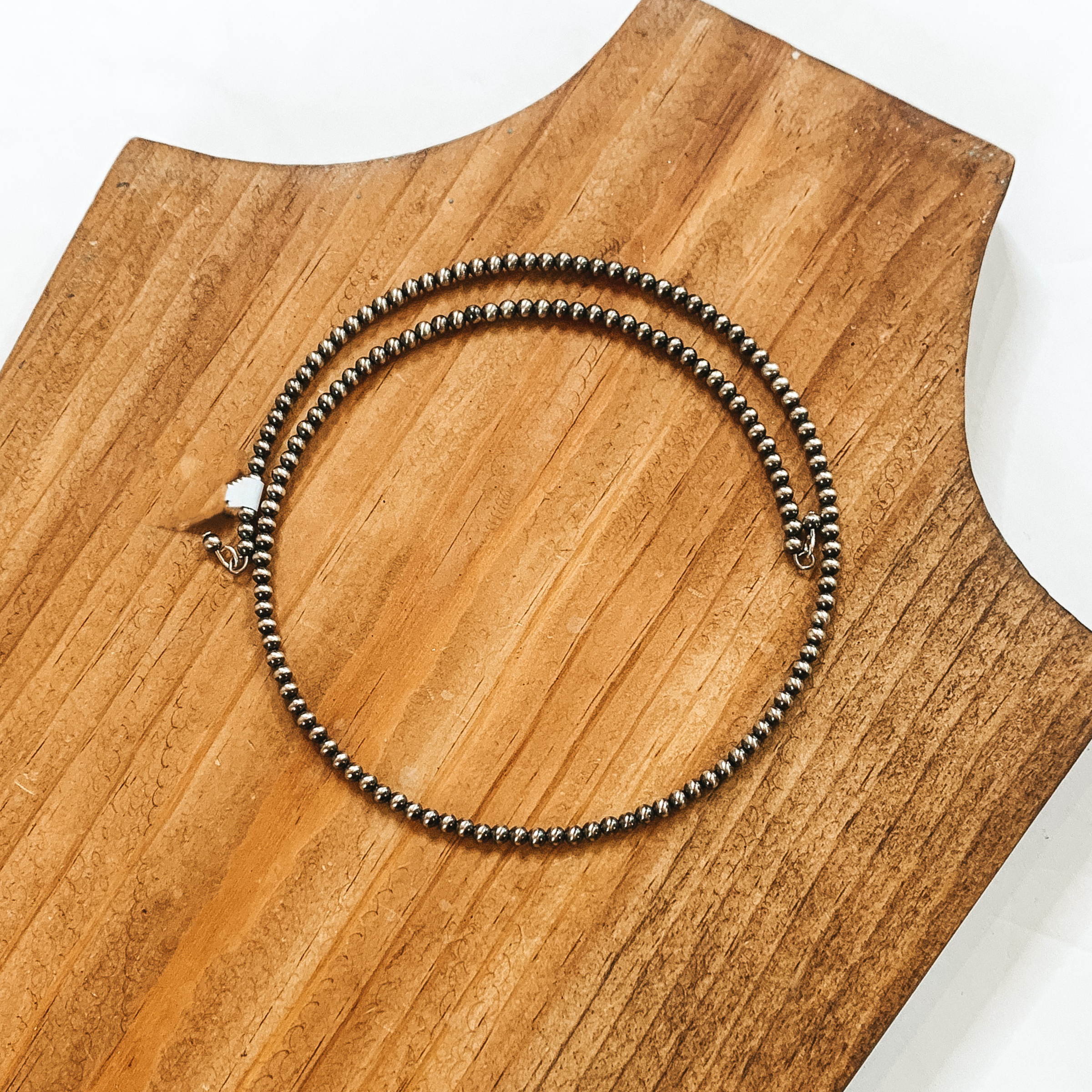 Silver beaded wrap necklace. This necklace is pictured on a wood necklace holder on a white background. 