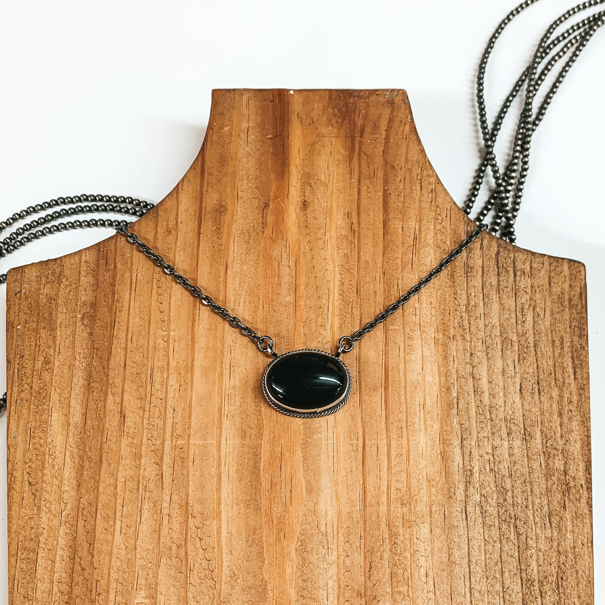 Silver chain necklace with an oval black stone pendant. This necklace is pictured on a wood block on a white background. 