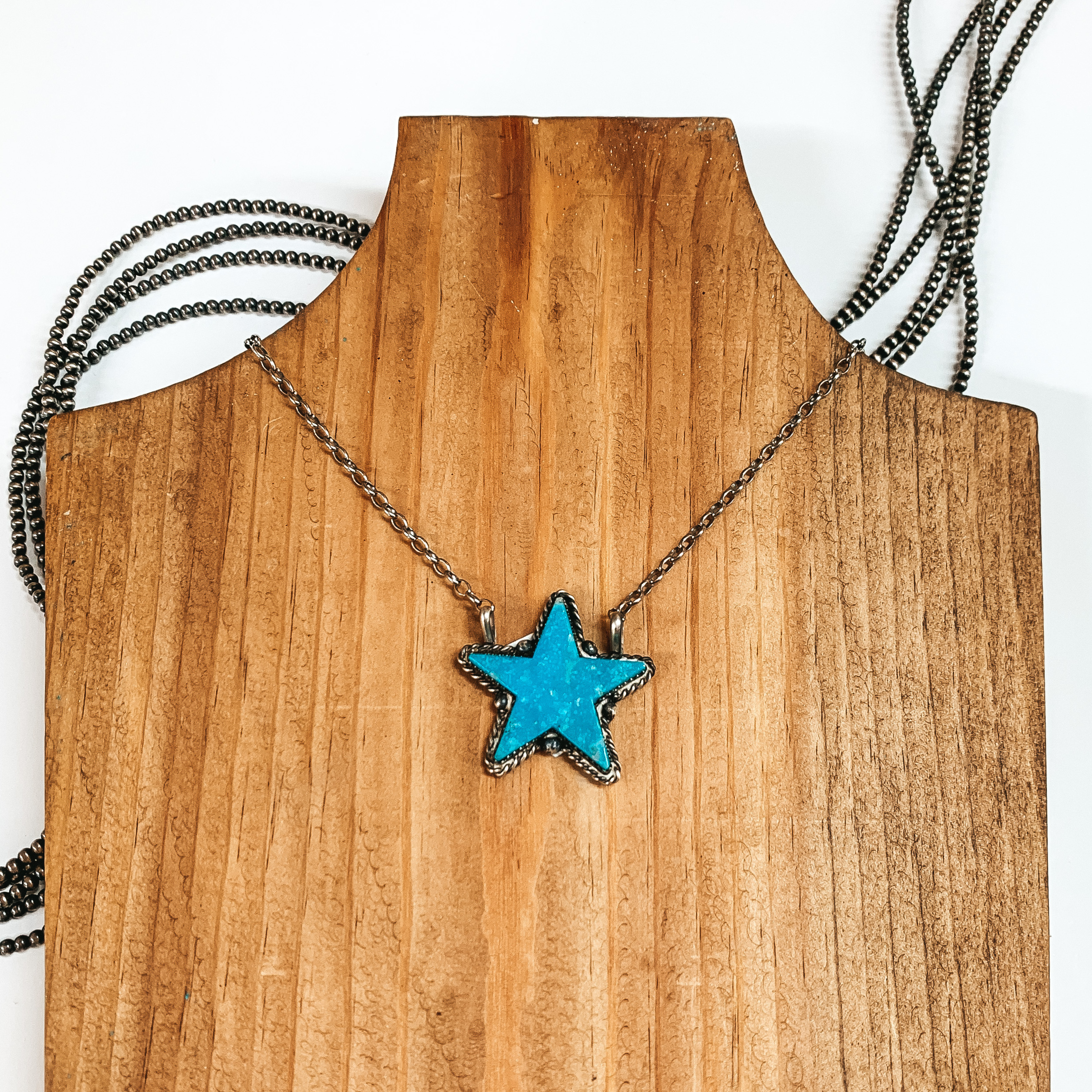 Silver chain necklace with turquoise star pendant. This necklace is pictured on a wood necklace holder on a white background. 