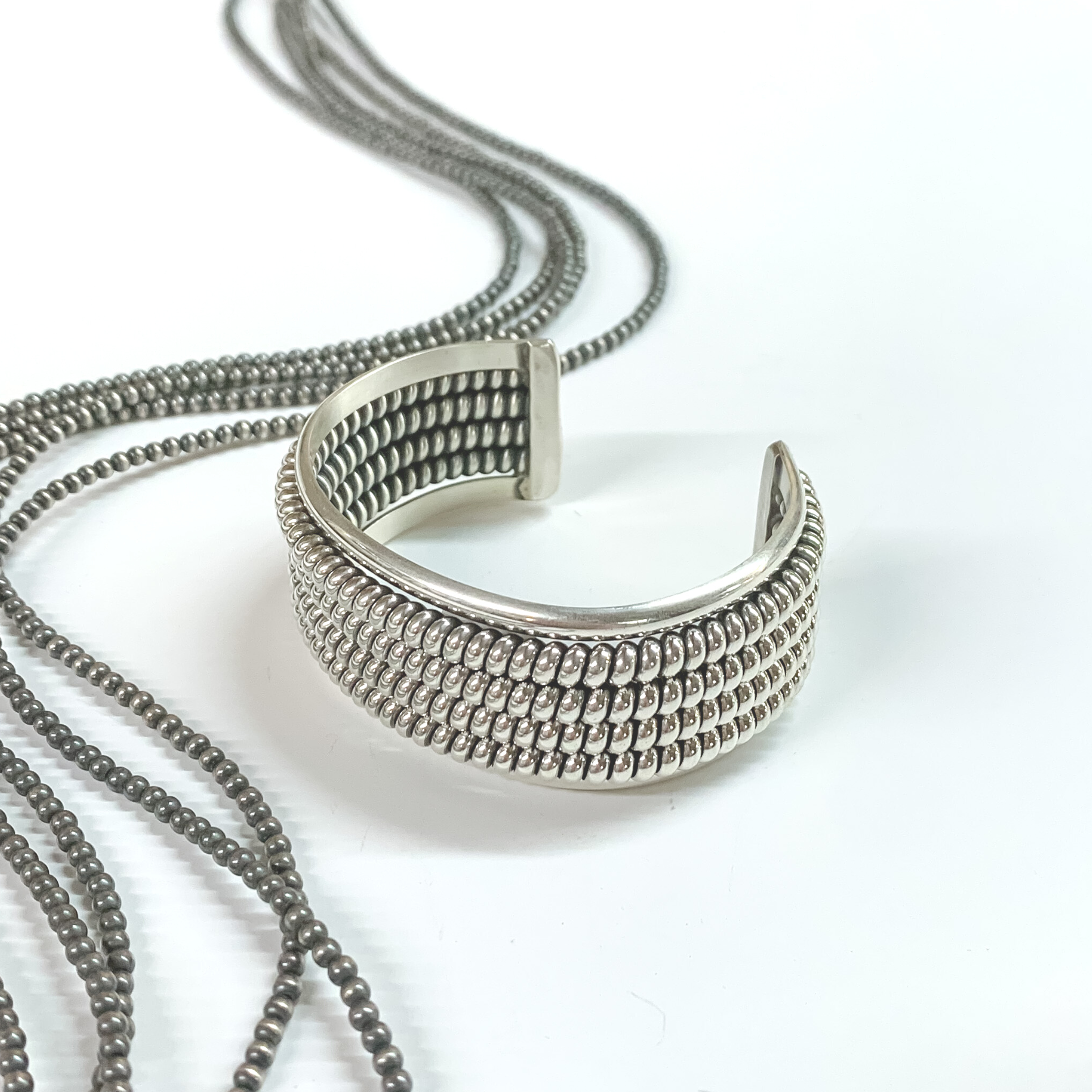 Silver cuff bracelet with a rope design. The rope design has four layers. This bracelet is pictured on a white background with silver beads on the left side. 