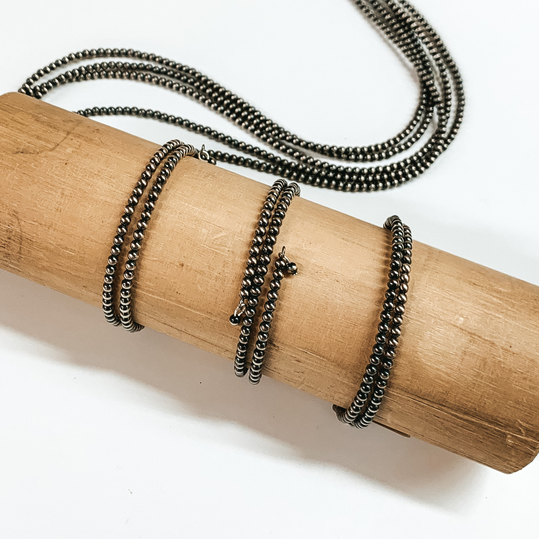 Three silver beaded wrap bracelets ppictured on a tan bracelet holder on a white background. 
