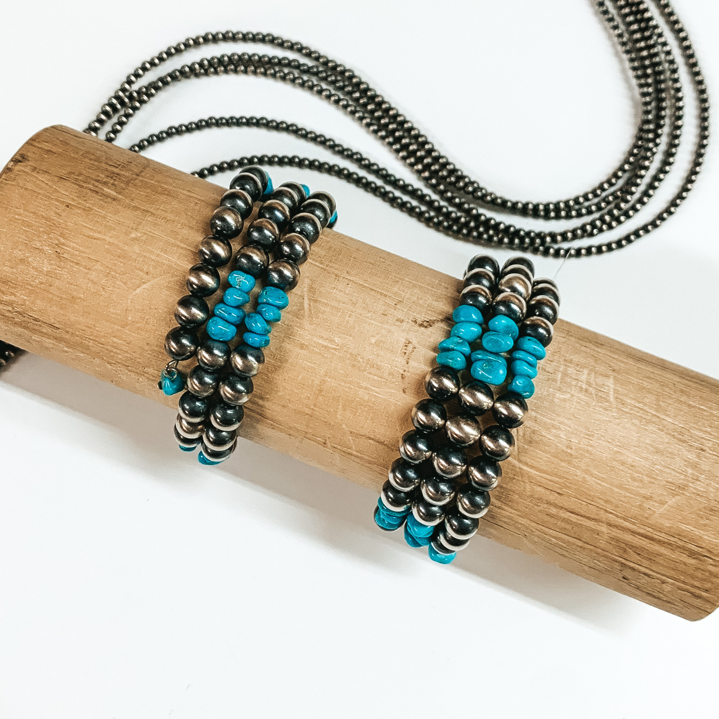 Three silver and turquoise beaded wrap bracelets pictured on a tan bracelet holder on a white background. 