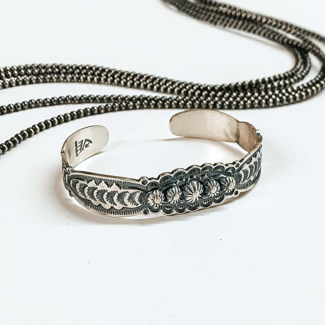 Silver cuff bracelet with a tooled design. These bracelets are pictured on a white background with silver beads at the top. 