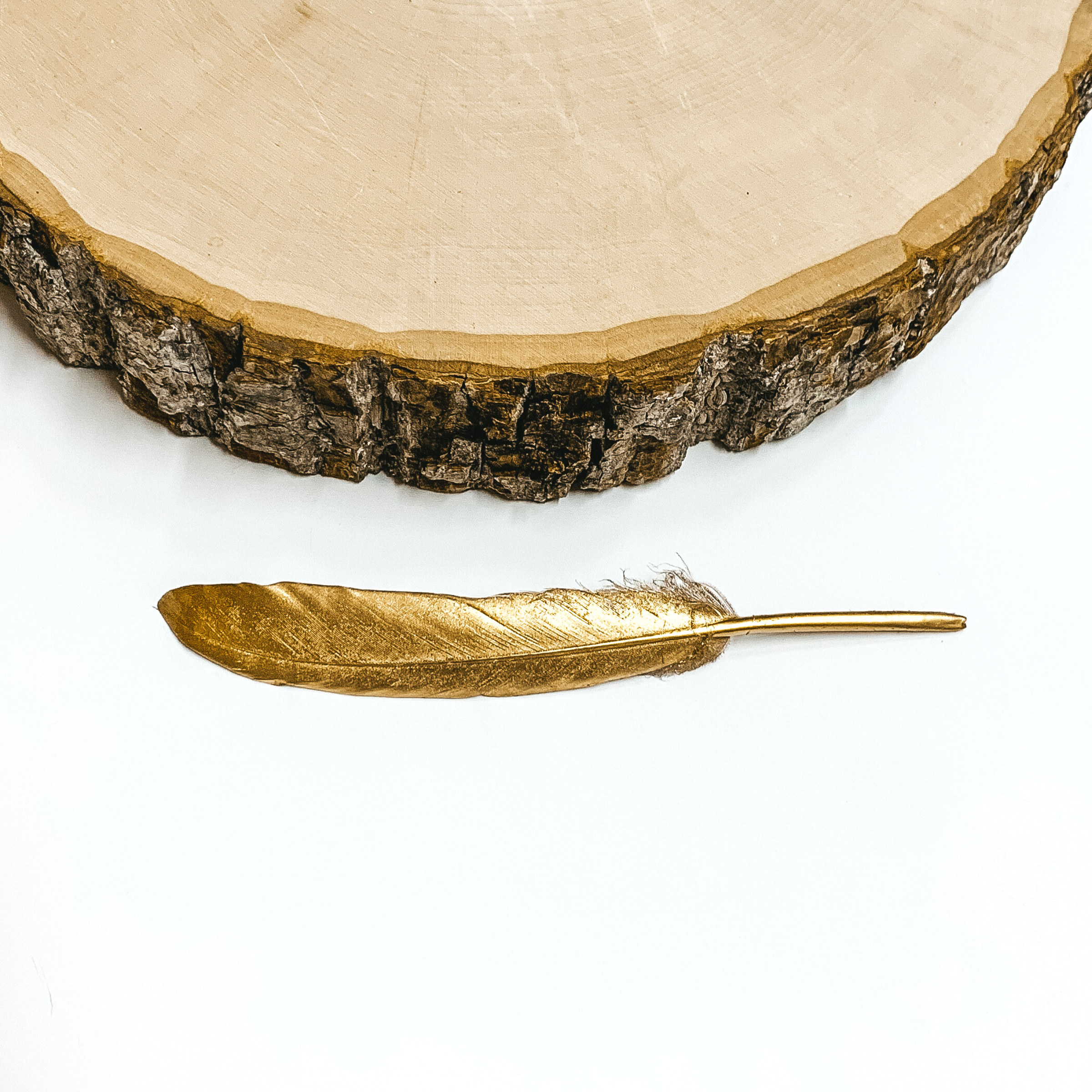 Gold feather pictured on on a white background with a block of wood above the feather. 