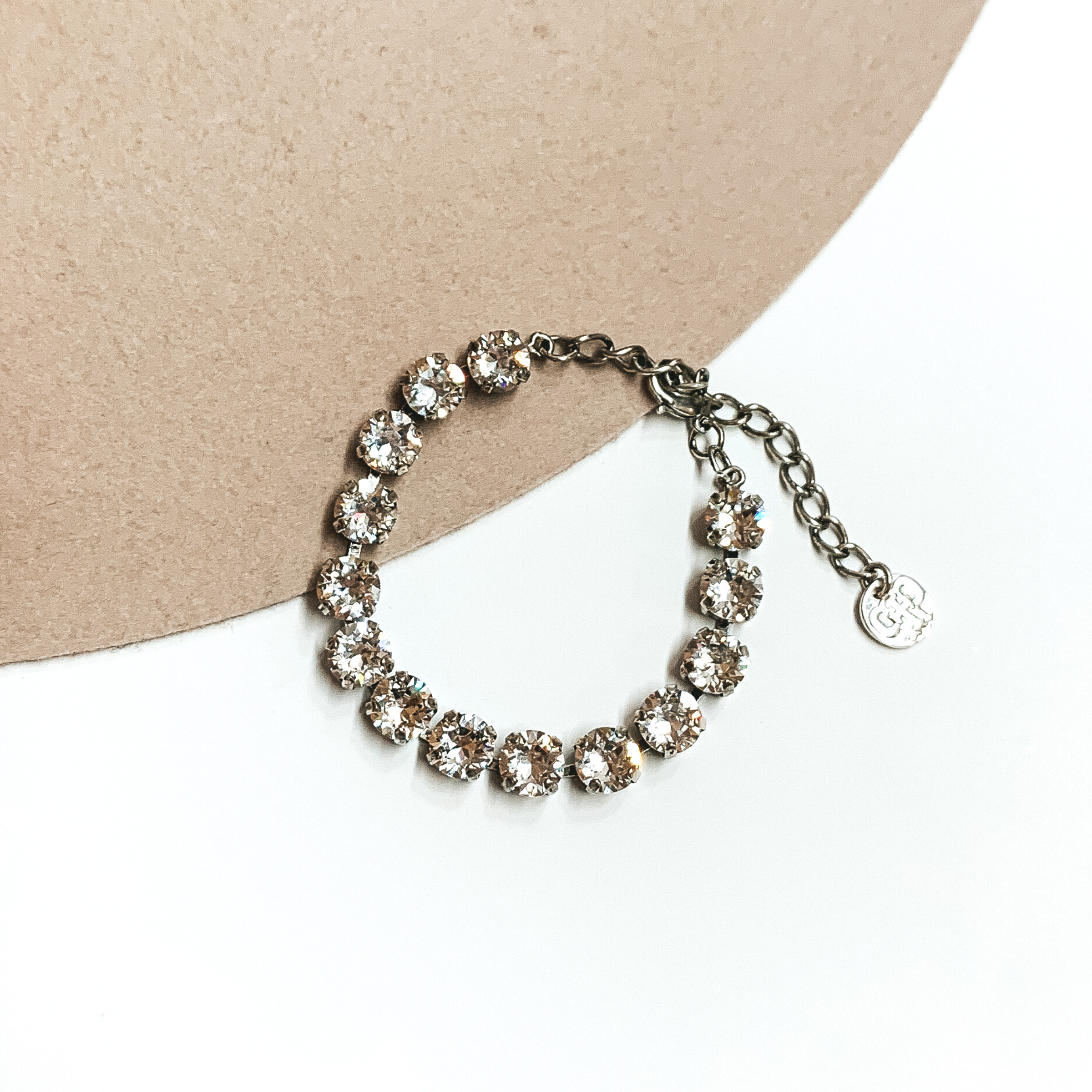 Circle, clear crystal bracelet with a silver backing. This bracelet is pictured on a white and tan background. 