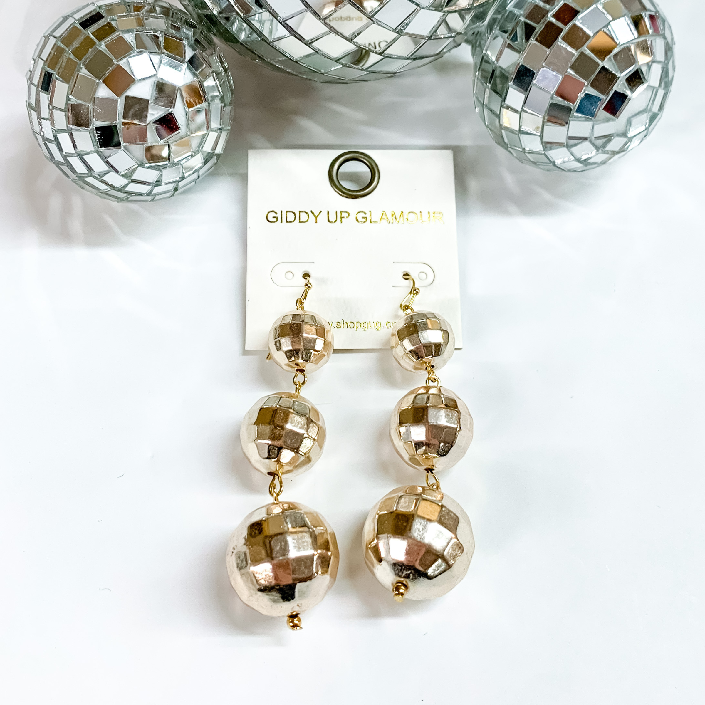 Three disco ball drop earrings in gold. These disco balls are in order of smallest to biggest at the bottom. These earring are pictured on a white background with disco balls at the top of the picture. 