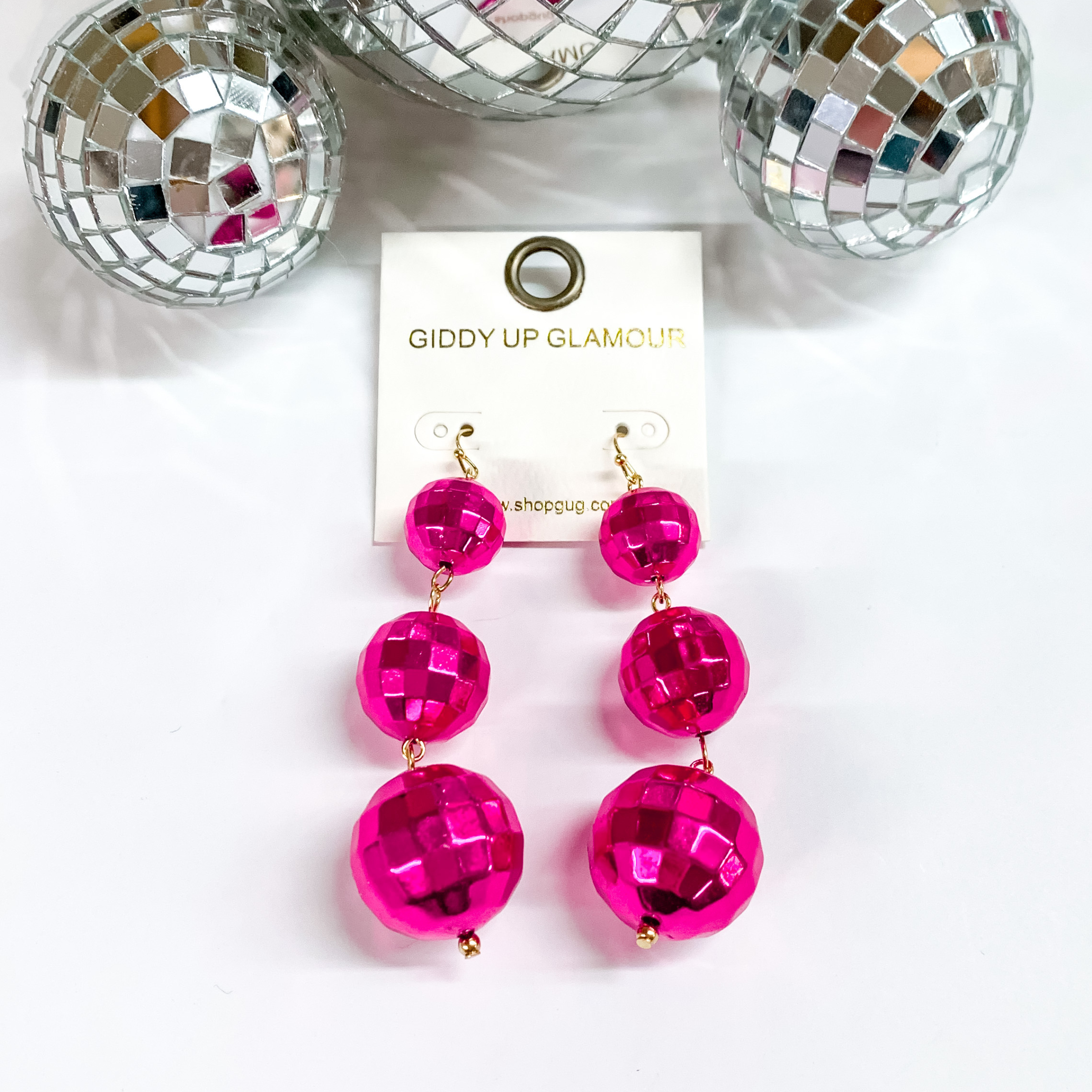 Three disco ball drop earrings in fuchsia. These disco balls are in order of smallest to biggest at the bottom. These earring are pictured on a white background with disco balls at the top of the picture. 