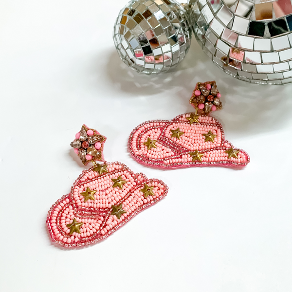 Light pink beaded cowboyd hat earrings that include gold star charms. These earrings are pictured on a white background with disco balls at the top.