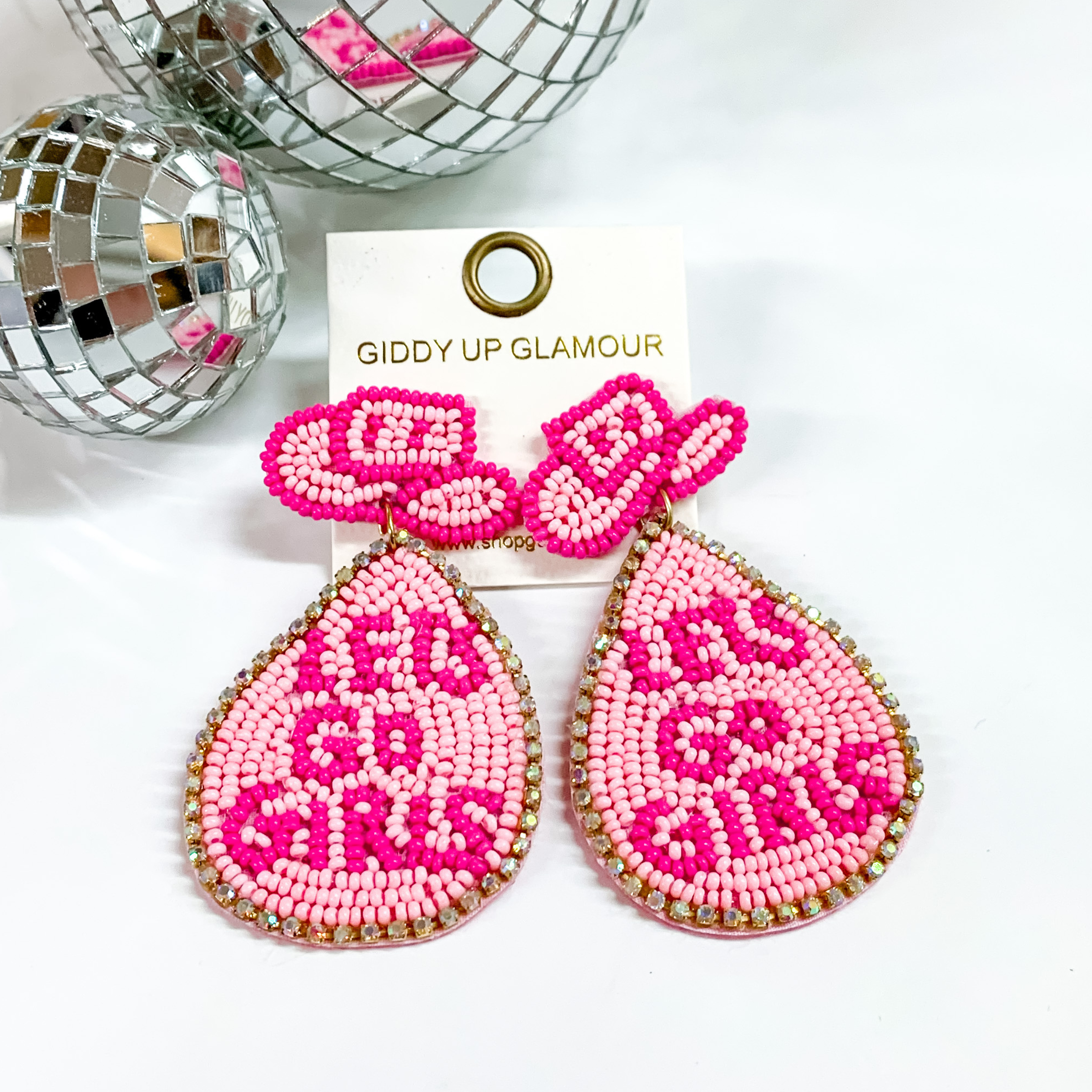 Pink beaded cowboy hat earrings with a pink hanging teardrop, The teardrop includes the words "LETS GO GIRLS" in dark pink and is outlined with ab crystals. These earrings are pictured on a white background with disco balls at the top.