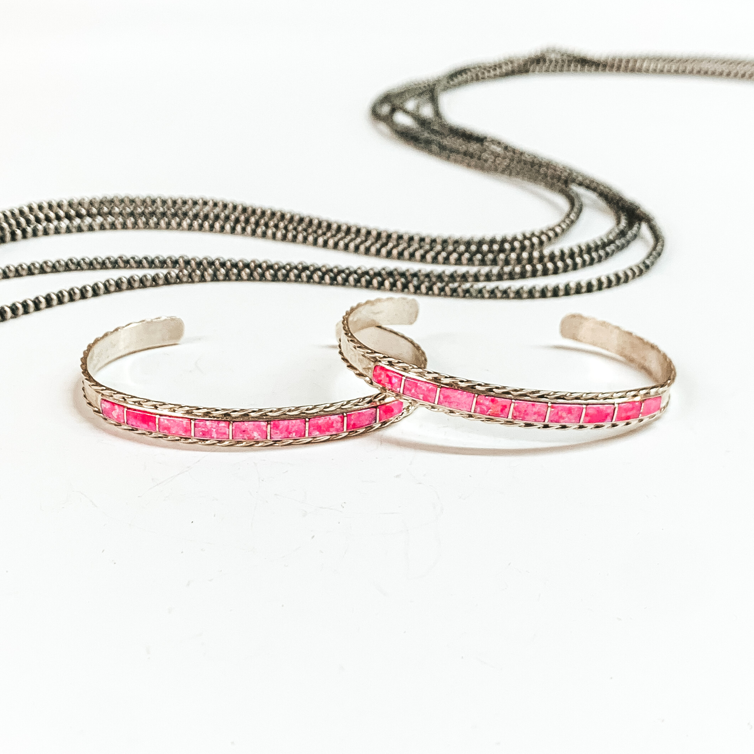 Two sterling silver cuff bracelets with nine pink opal stone inlay. These bracelets are pictured on a white background with silver beads above the bracelets. 