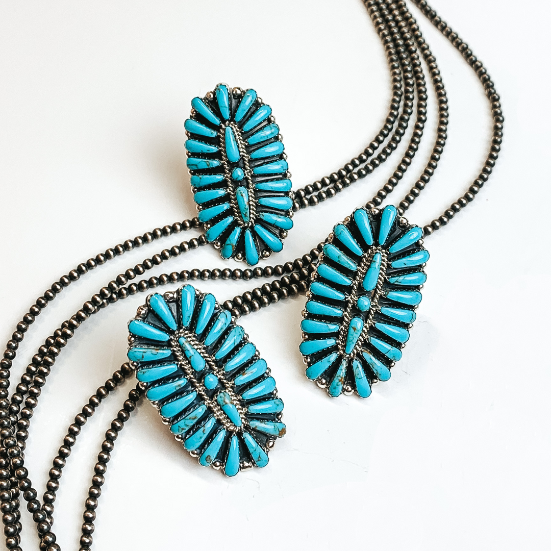 Oval turquoise stone cluster ring. There are three rings pictured on a white background and silver beads through the middle of the picture. 