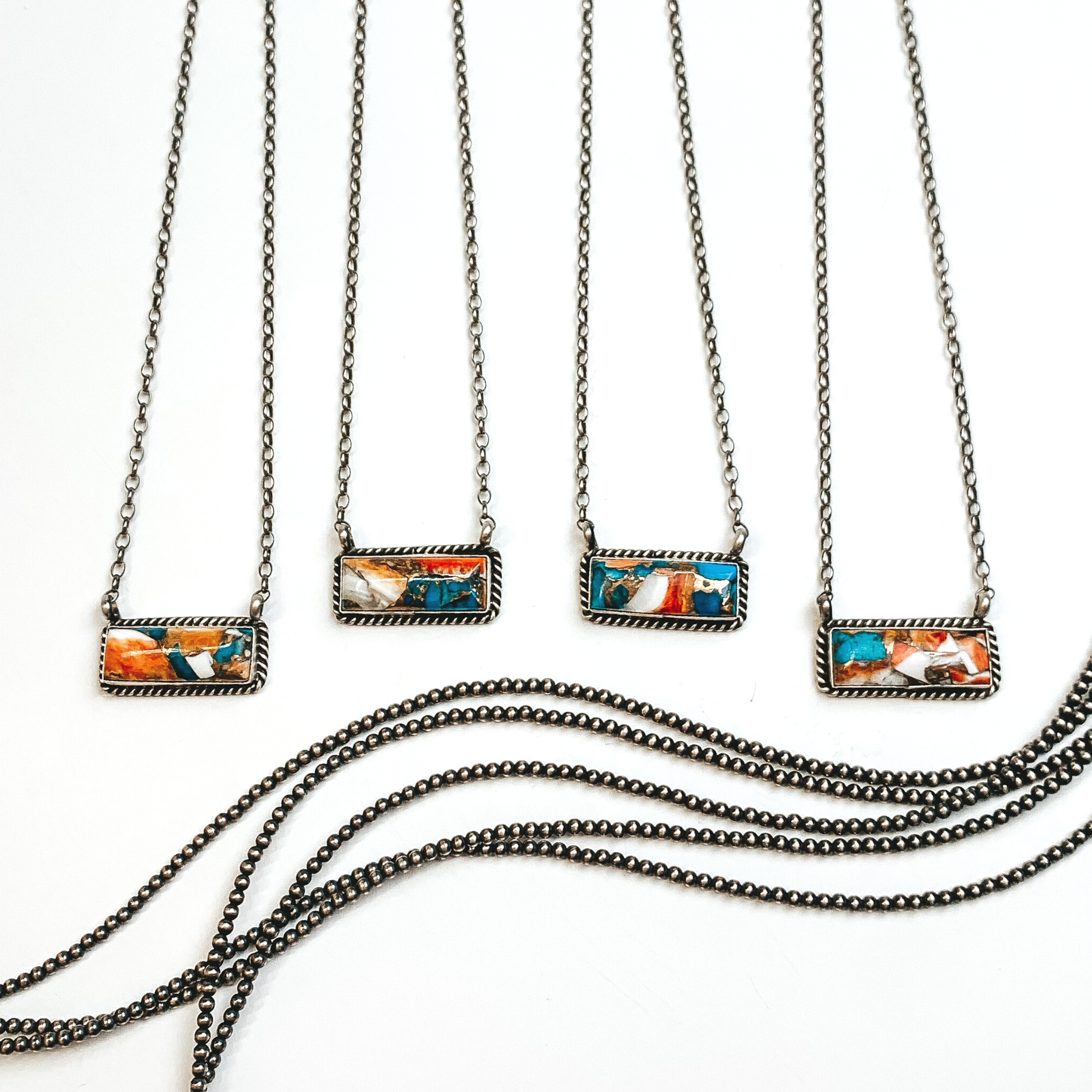 Four silver chain necklaces with rectangle bars that have a spiny oyster and turquoise remix stone. These necklaces are pictured on a white background with silver beads under the necklaces. 