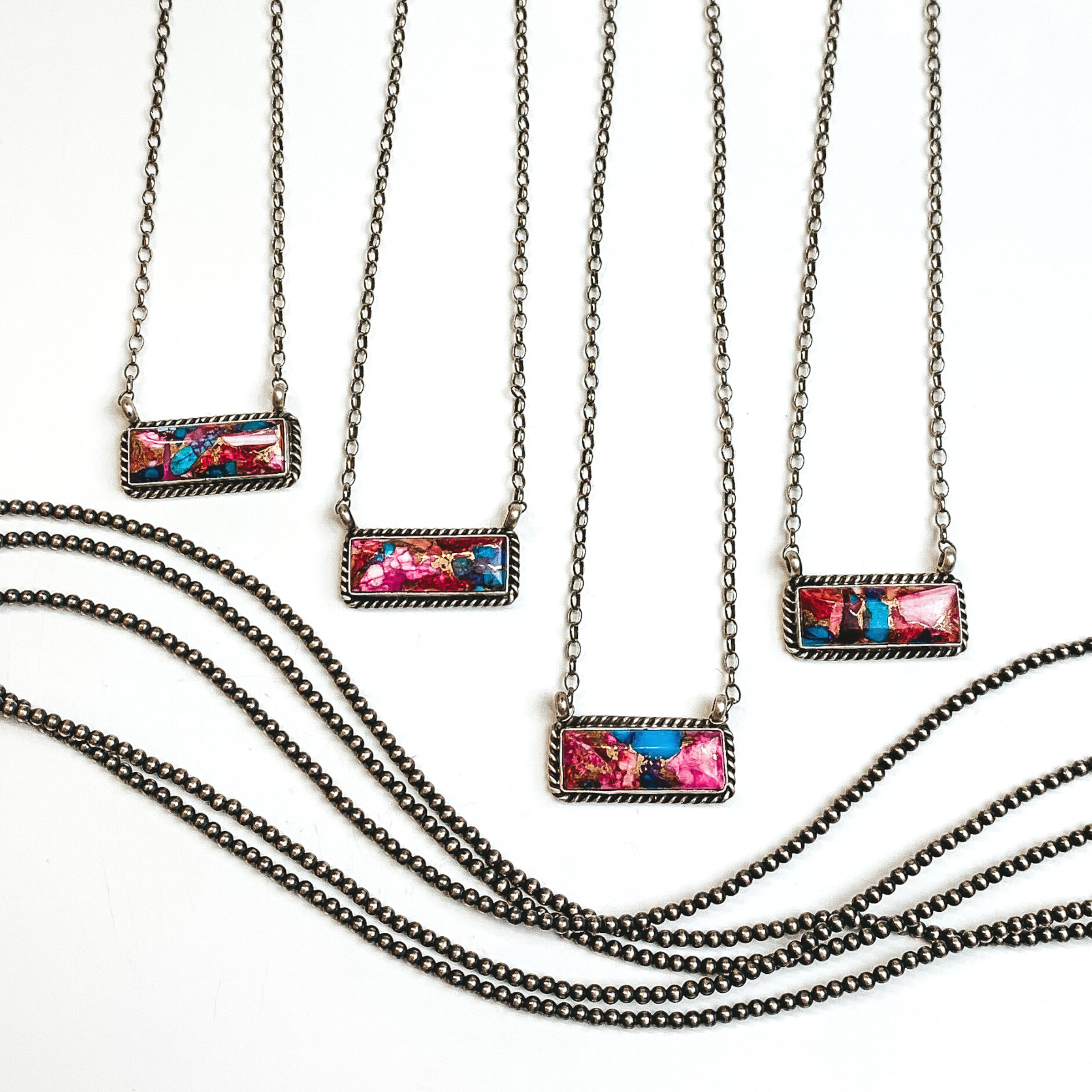 Four silver chain necklaces with rectangle bars that have a pink mojave and turquoise remix stone. These necklaces are pictured on a white background with silver beads under the necklaces. 
