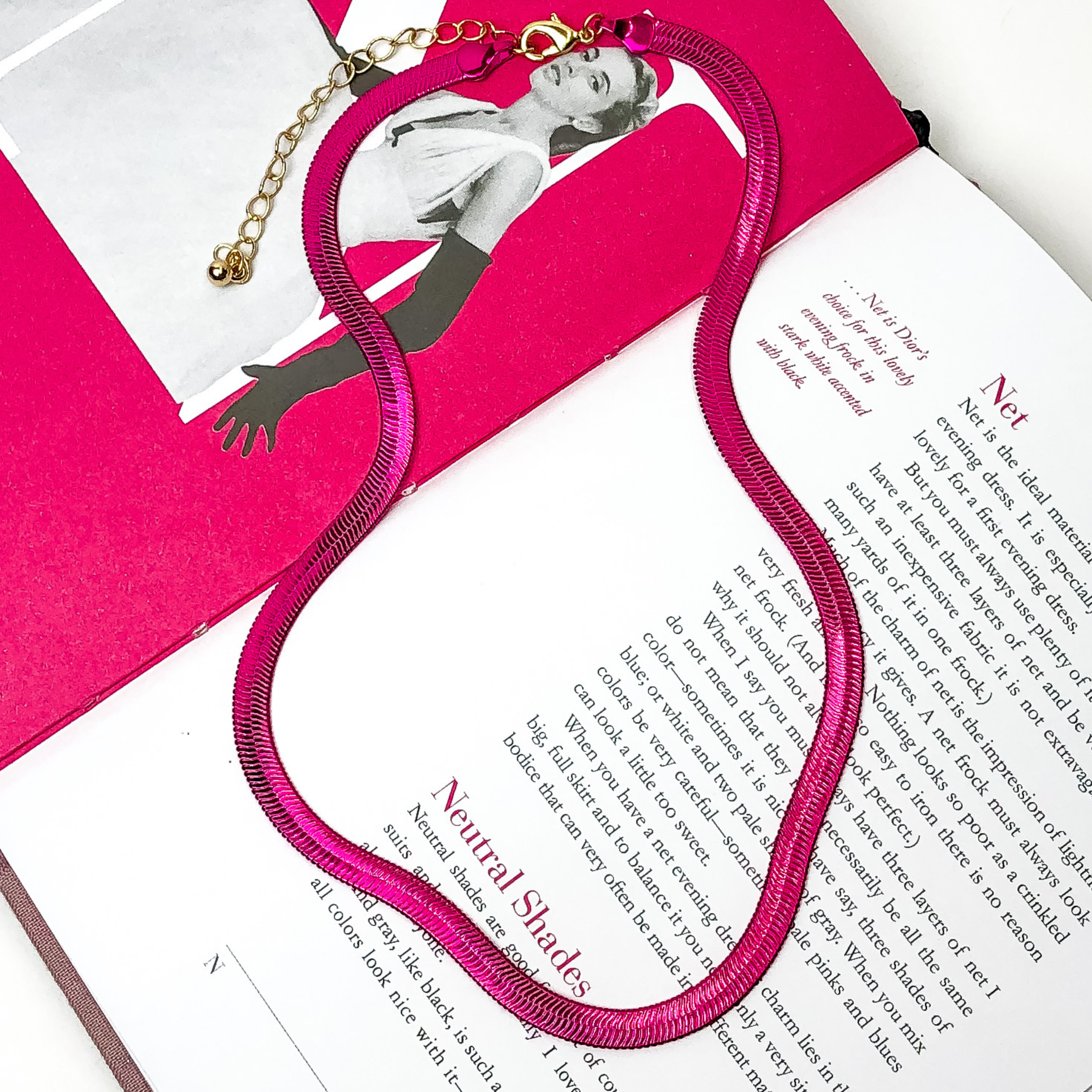 Hot pink snake chain with a gold extender. This necklace is on a opened book, on a white background. 